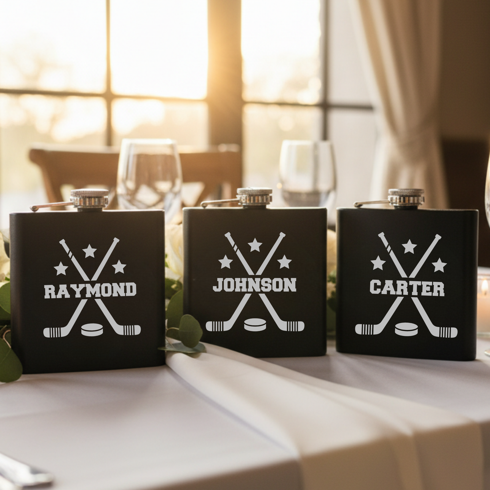 Three black matte flasks with laser-etched hockey design featuring crossed sticks, puck, and stars, personalized with sample names "Raymond," "Johnson," and "Carter