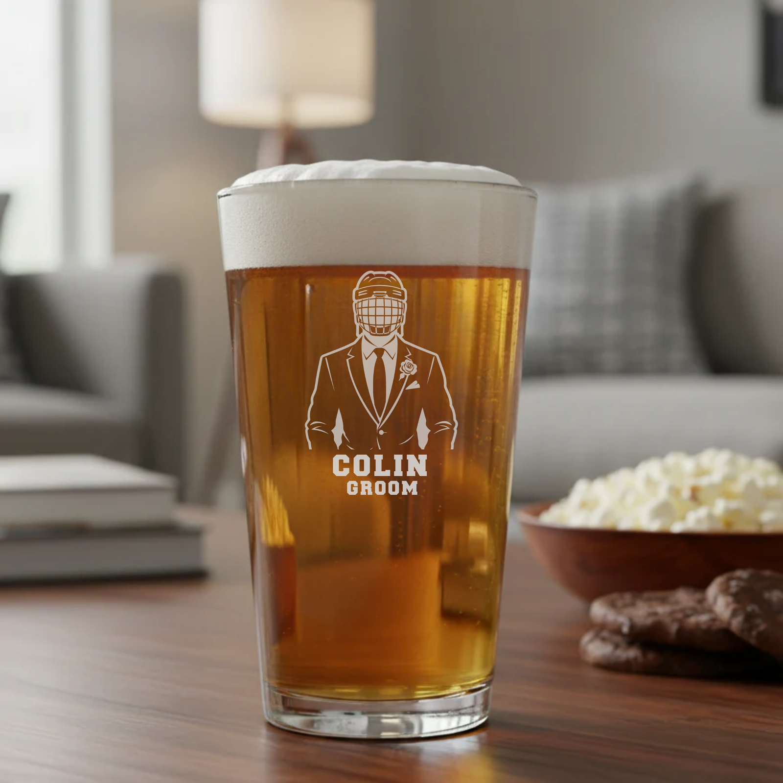 Tall pint glass filled with amber beer, topped with white foam, laser-etched with illustration of man in hockey helmet and suit labeled "COLIN GROOM