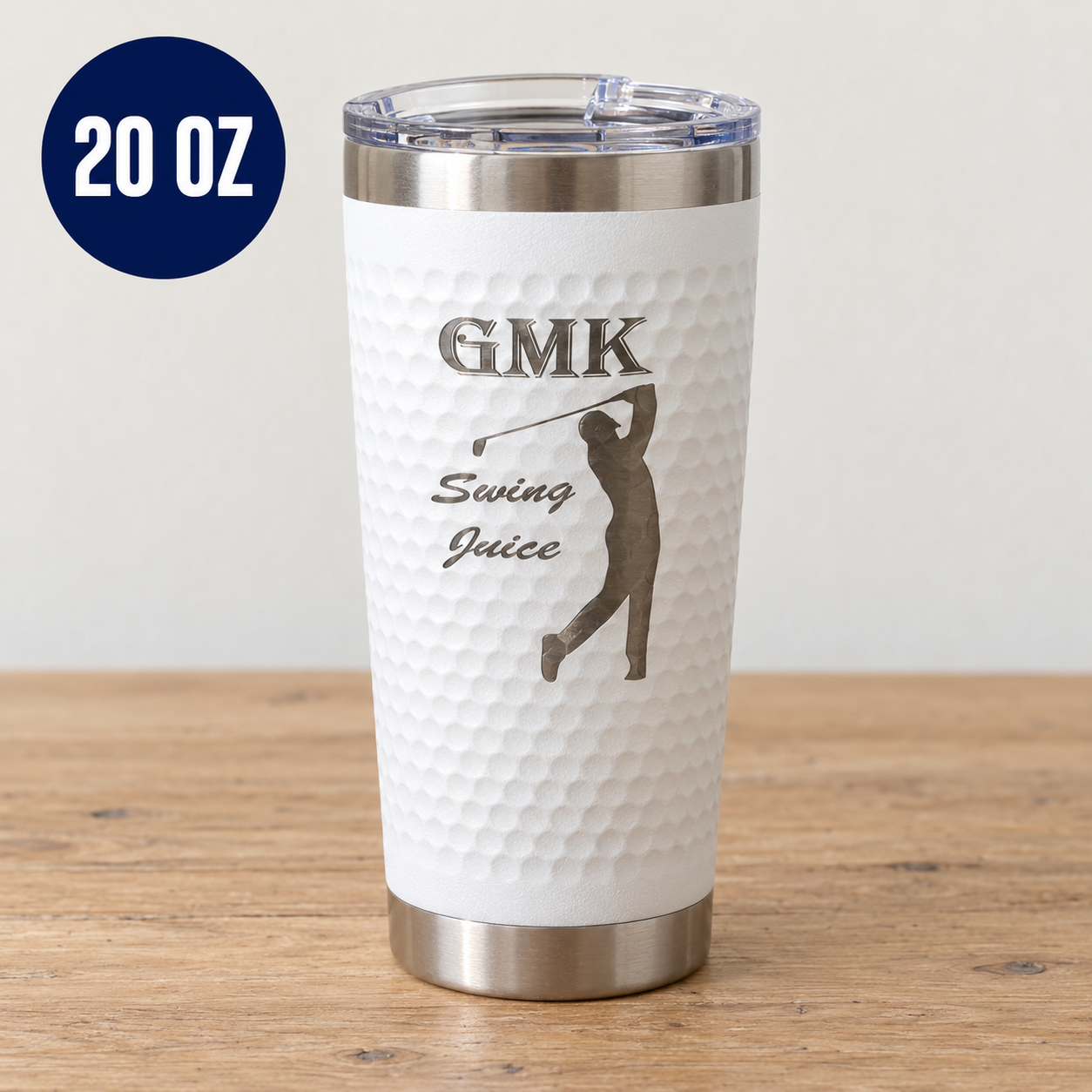 A 20 oz white stainless steel tumbler with a textured dimpled finish, featuring a black laser-engraved golf player silhouette and the text 'GMK Swing Juice'. The tumbler is shown on a wooden table against a neutral wall, with a blue '20 OZ' badge in the top left corner.