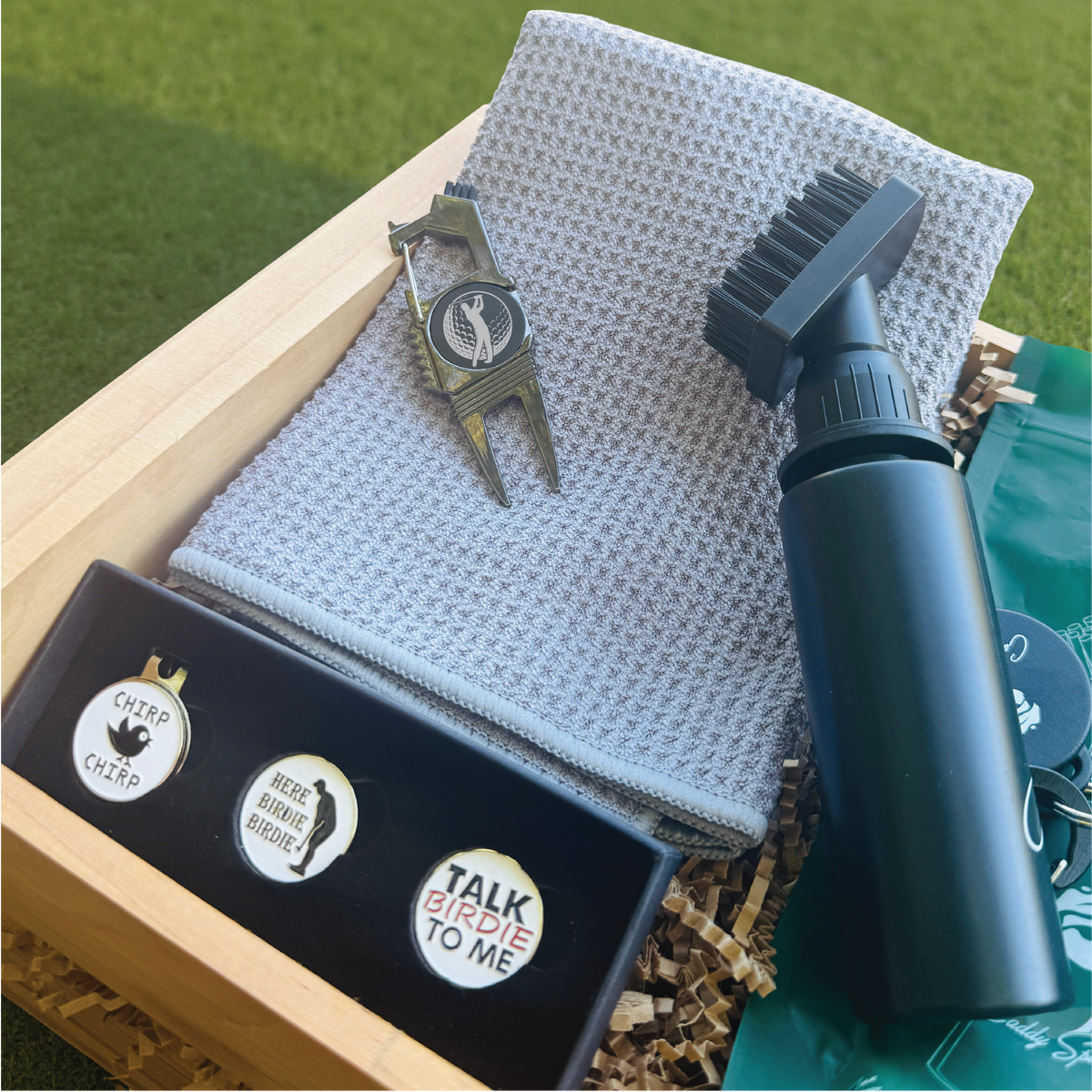 Golf care products including a brush, towel, and accessories on a green grass background