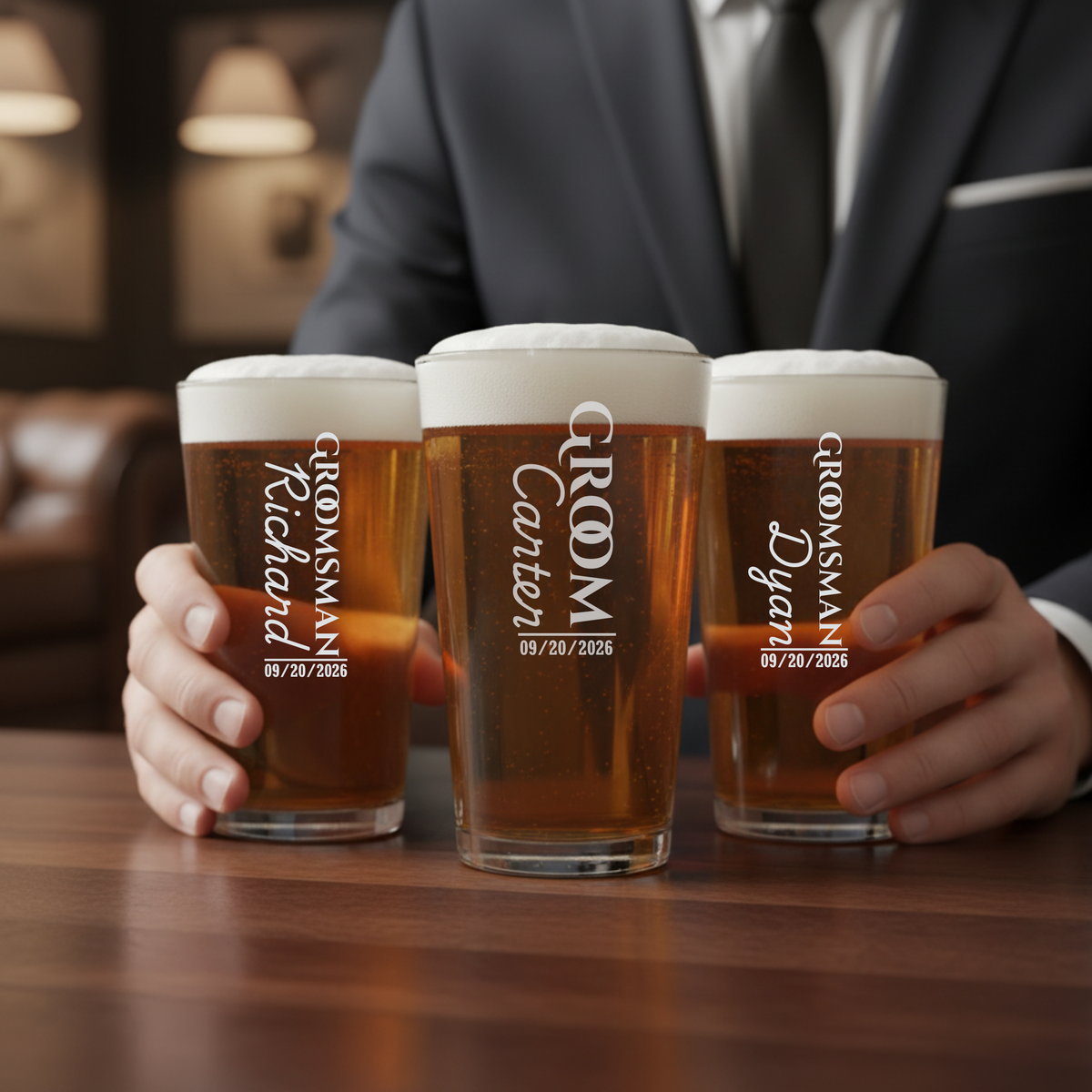Three pint glasses filled with beer, each engraved with sample text "GROOM'S Crew" and date "09/20/2026", held by a man in formal attire