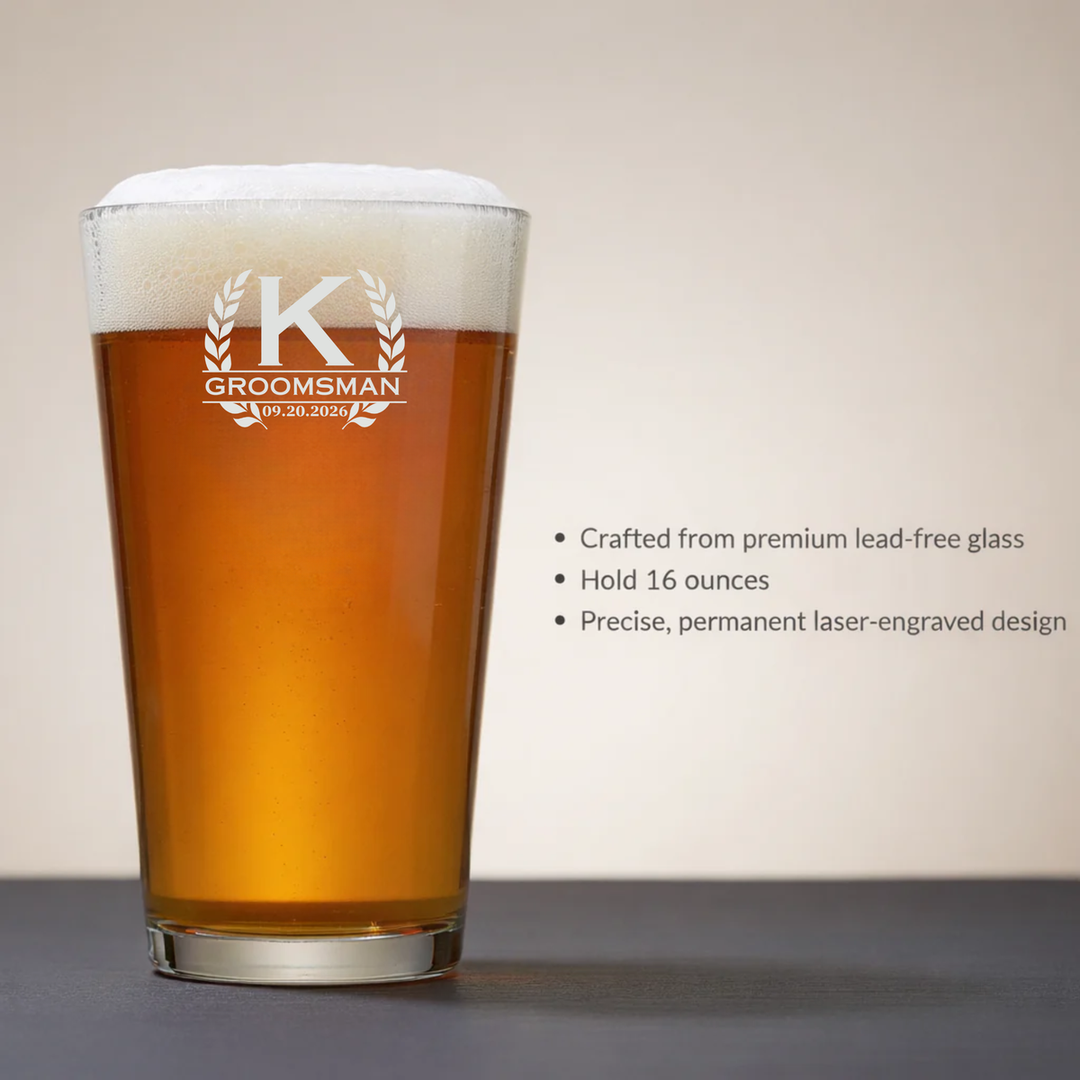 16-ounce pint glass laser-engraved with sample monogram "K GROOMSMAN" and laurel wreath design with date 09.20.2026, filled with beer