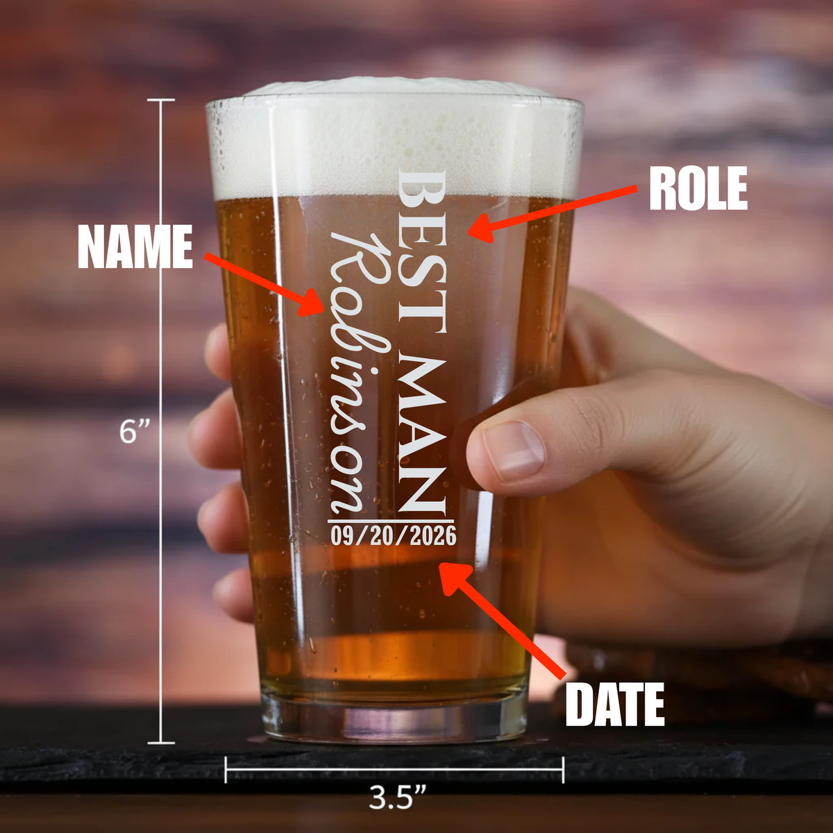 Beer pint glass filled with amber beer, held in hand, showing sample engraving with "BEST MAN," groomsman name, wedding role, and date 09/20/2026