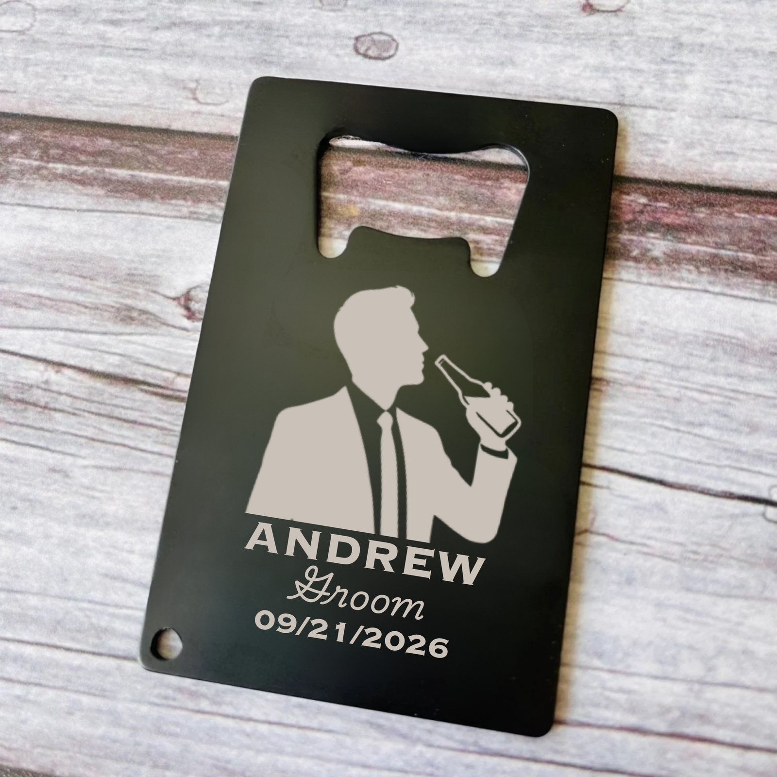 Black stainless steel card opener laser-engraved with sample personalization showing groomsman silhouette, name "ANDREW," title "Groom," and wedding date "09/21/2026