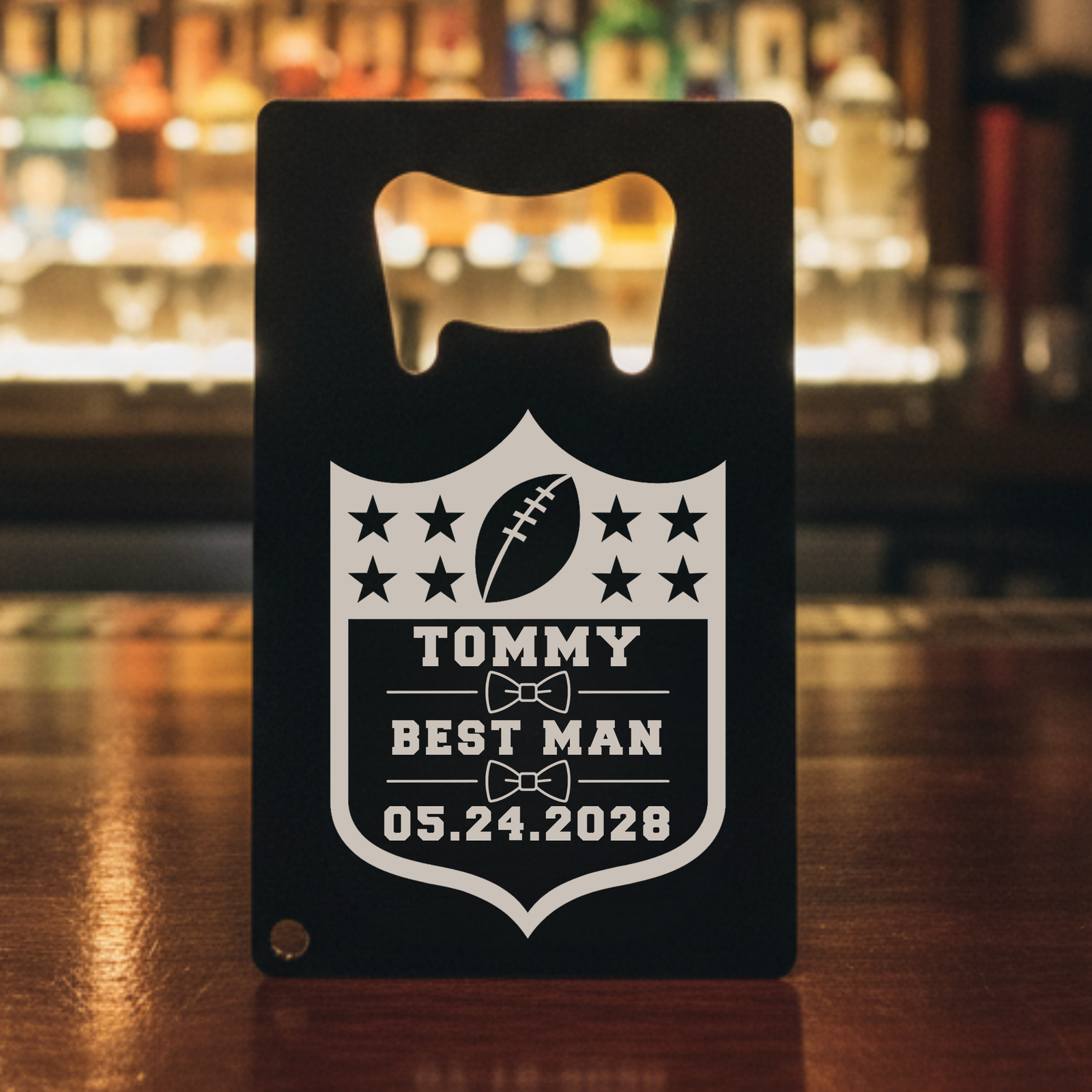 Black stainless steel bottle opener with engraved football shield design featuring stars, football icon, and personalized text sample reading "TOMMY BEST MAN 05.24.2028