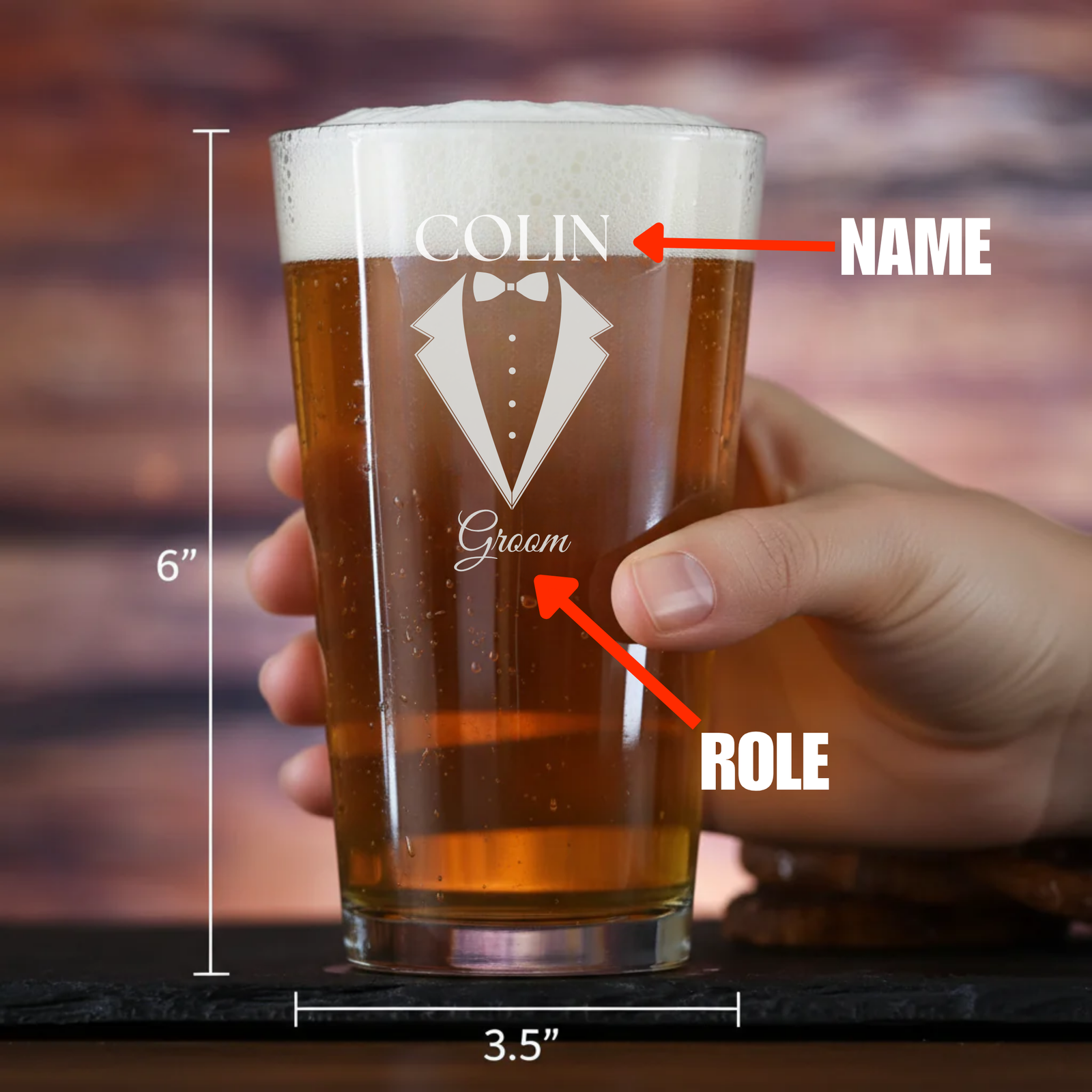 Pint glass filled with beer, engraved with sample personalization showing name "COLIN" at top, "Groom" text, and tuxedo bowtie design, held in hand, 6 inches tall