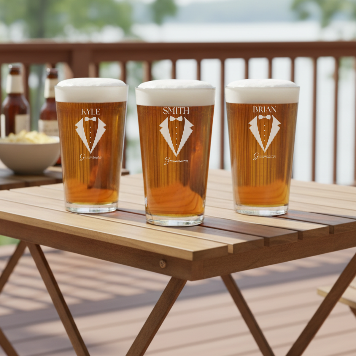 Three personalized pint glasses with sample names Kyle, Smith, and Brian engraved with tuxedo and bowtie design and "Groomsman" text, filled with beer on outdoor table.