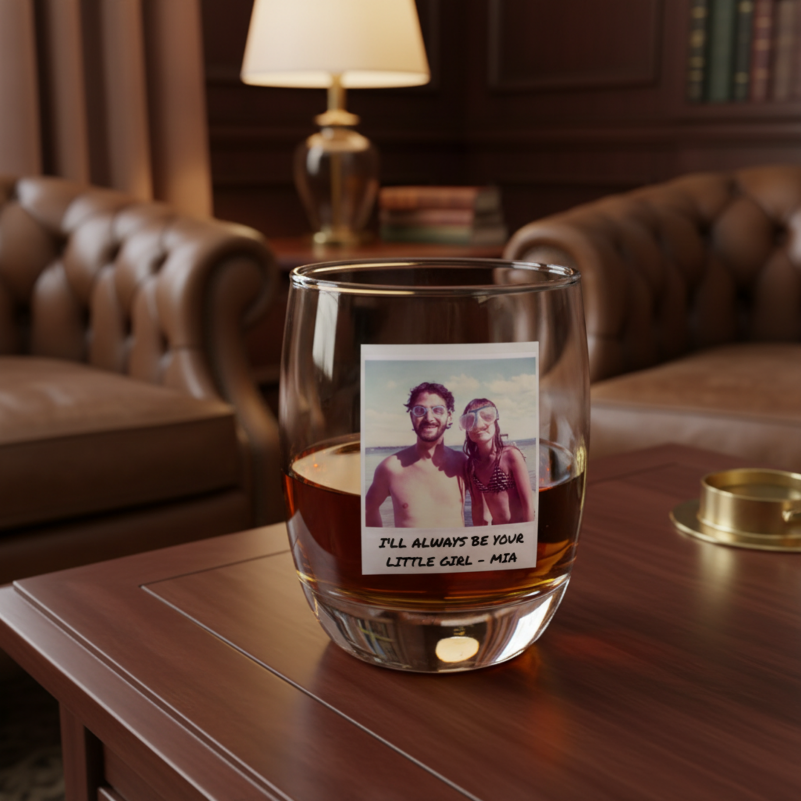 Whiskey glass filled with amber liquid, personalized with a sample photo of two people and custom text "I'll Always Be Your Little Girl - Mia", displayed on wooden table in elegant study room setting.