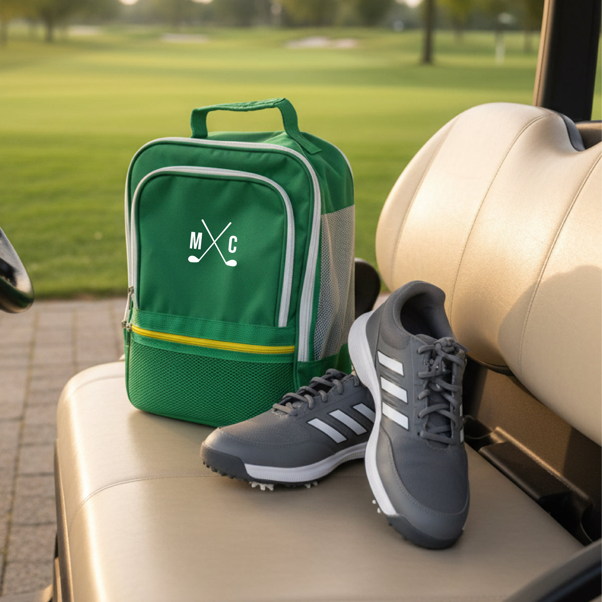 Green golf shoe bag with crossed golf club monogram sample "MC" and yellow trim, displayed on golf cart seat next to black golf shoes