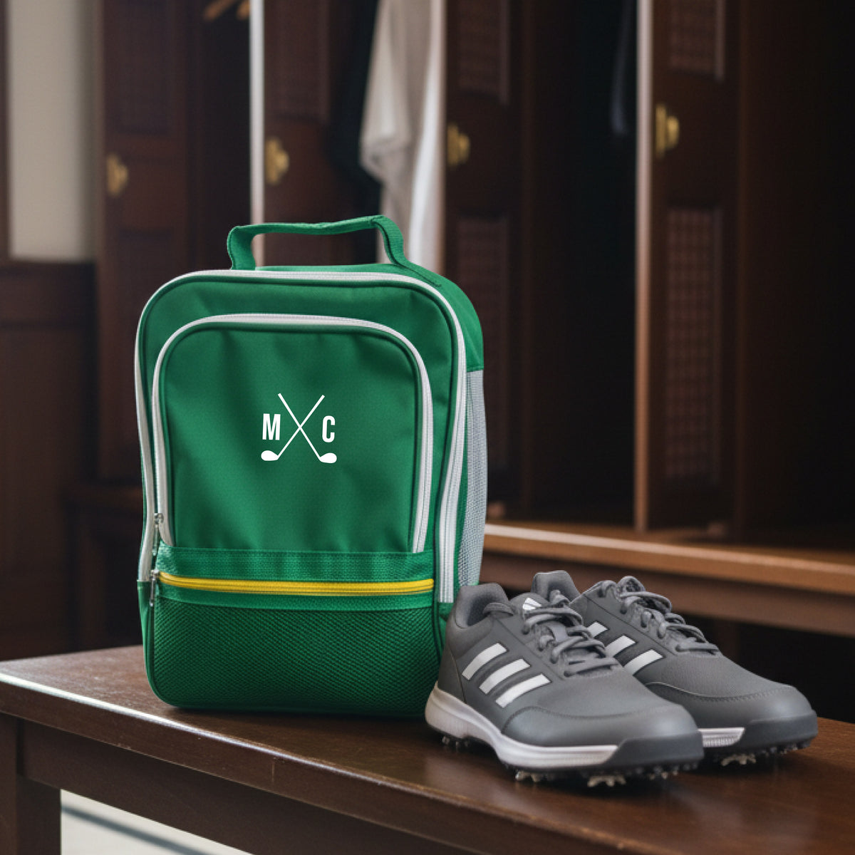 Green golf shoe bag with sample monogram "MXC" and crossed clubs design, displayed alongside gray golf shoes on wooden table