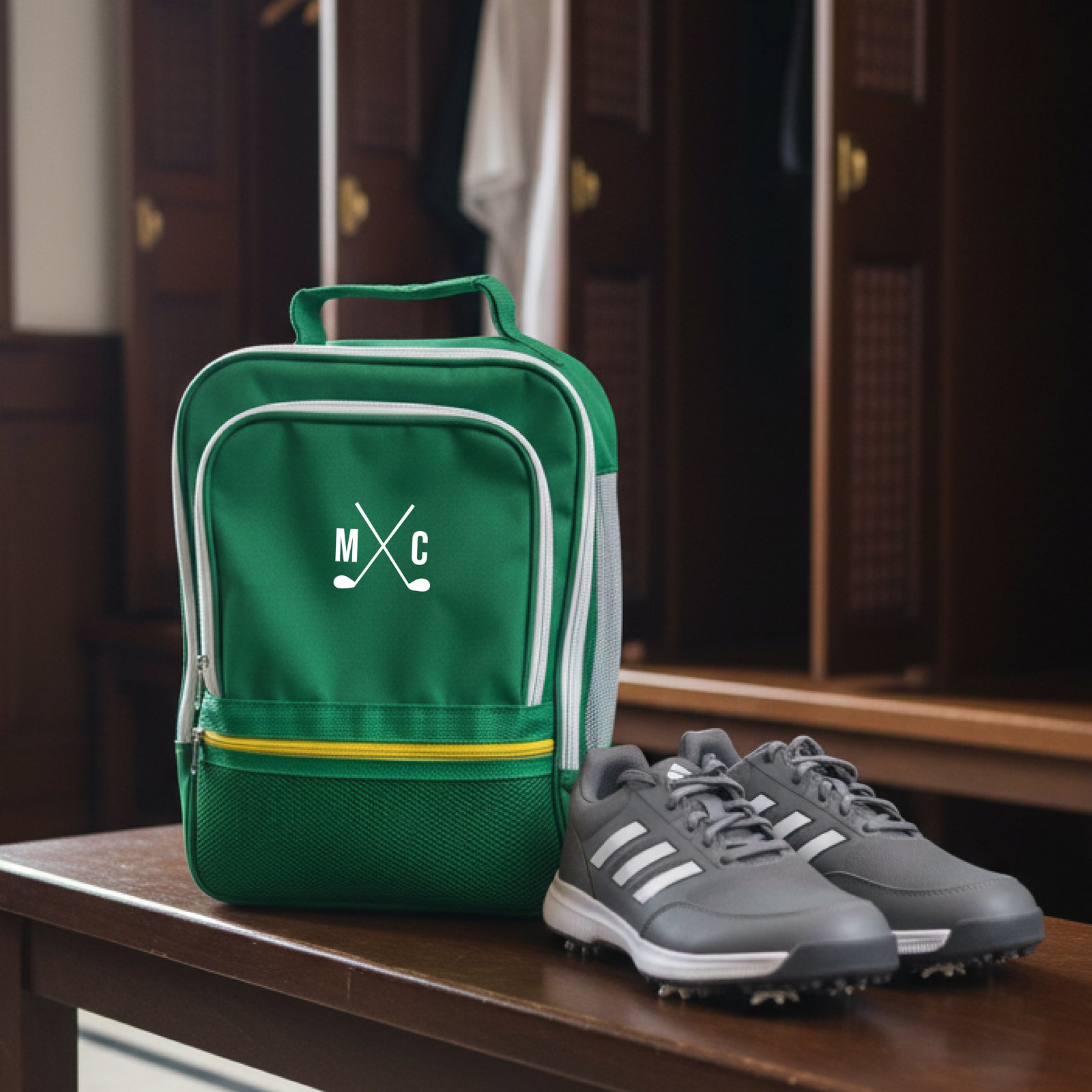 Green golf shoe bag with sample monogram "MXC" and crossed clubs design, displayed alongside gray golf shoes on wooden table
