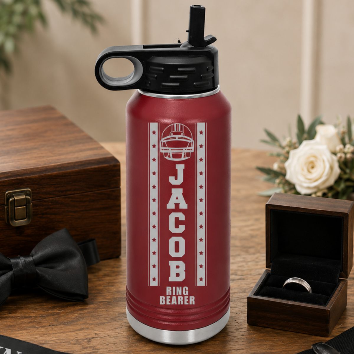 Red insulated water bottle with black spout engraved with football helmet, "JACOB" name sample, and "RING BEARER" text, displayed with wooden box and ring box.