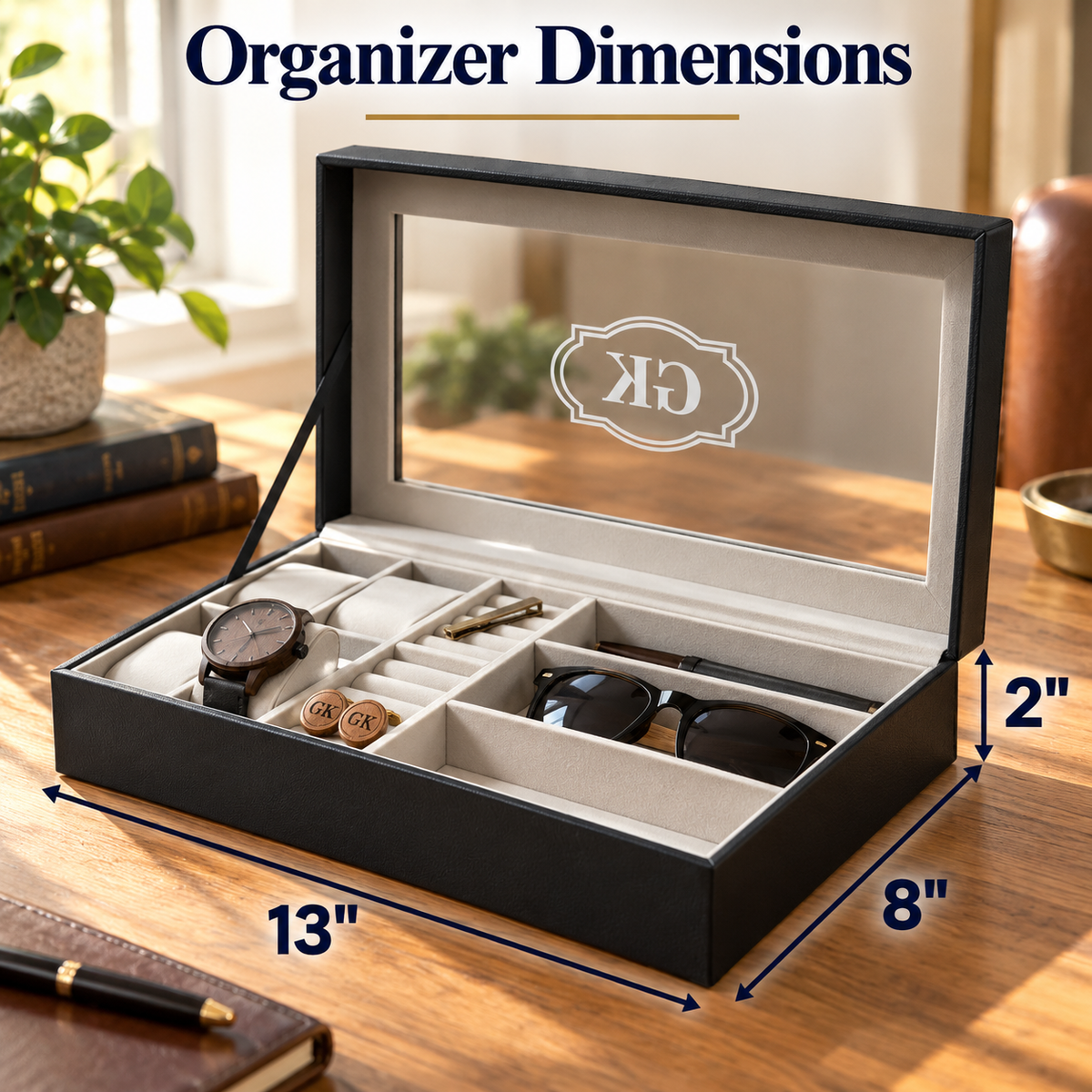 Open black organizer box with a clear lid and interior compartments, shown on a wooden desk with dimension labels reading 13 inches by 8 inches and a 2-inch height. The box contains a watch, sunglasses, and small accessories, and the image includes the text 'Organizer Dimensions' and a monogram on the lid.