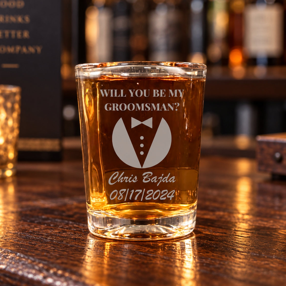 Brew shooter shot glass of whiskey on a bar, engraved WILL YOU BE MY GROOMSMAN? over a tuxedo emblem with a bow tie, a name in script and a date below