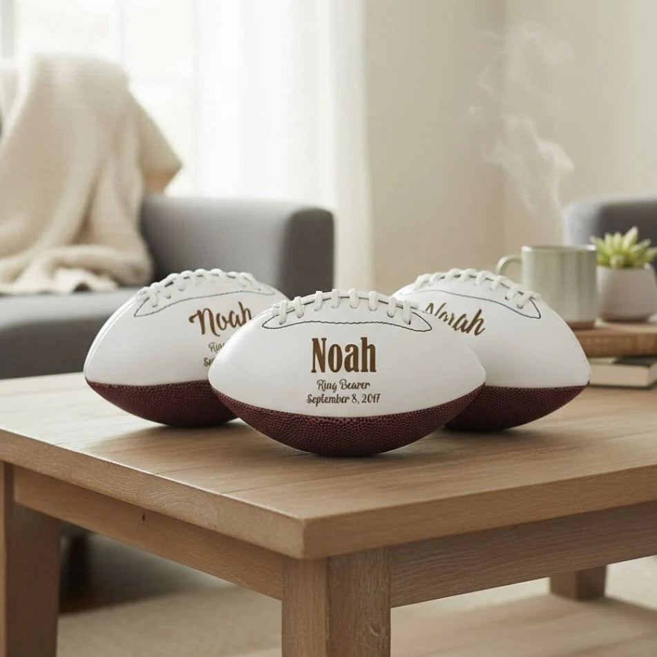 Three personalized proposal footballs on a wooden coffee table in a living room setting.