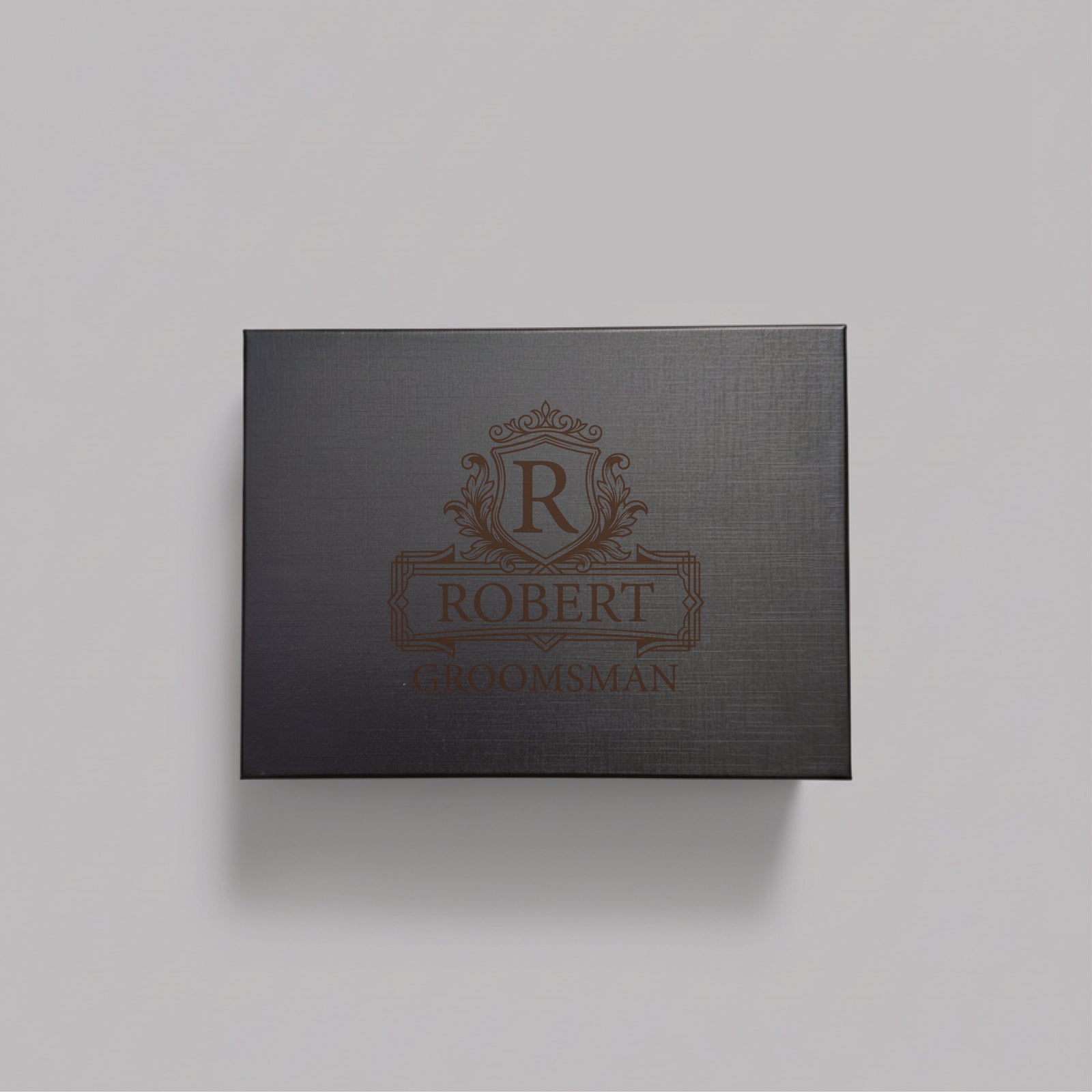 Black gift box with ornate heraldic crest and sample personalization engraved with name "ROBERT" and title "GROOMSMAN