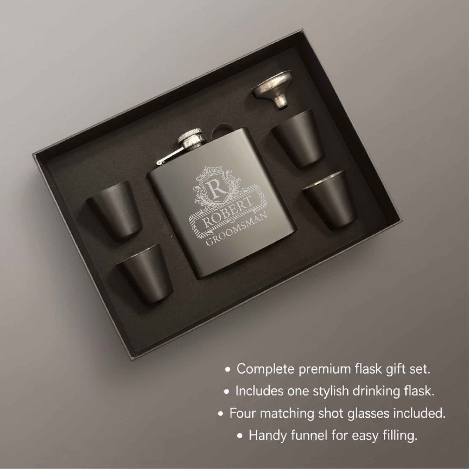 Flask gift set in black box containing stainless steel flask engraved with sample text "Robert Groomsman" with decorative crest, four matching shot glasses, and metal funnel.