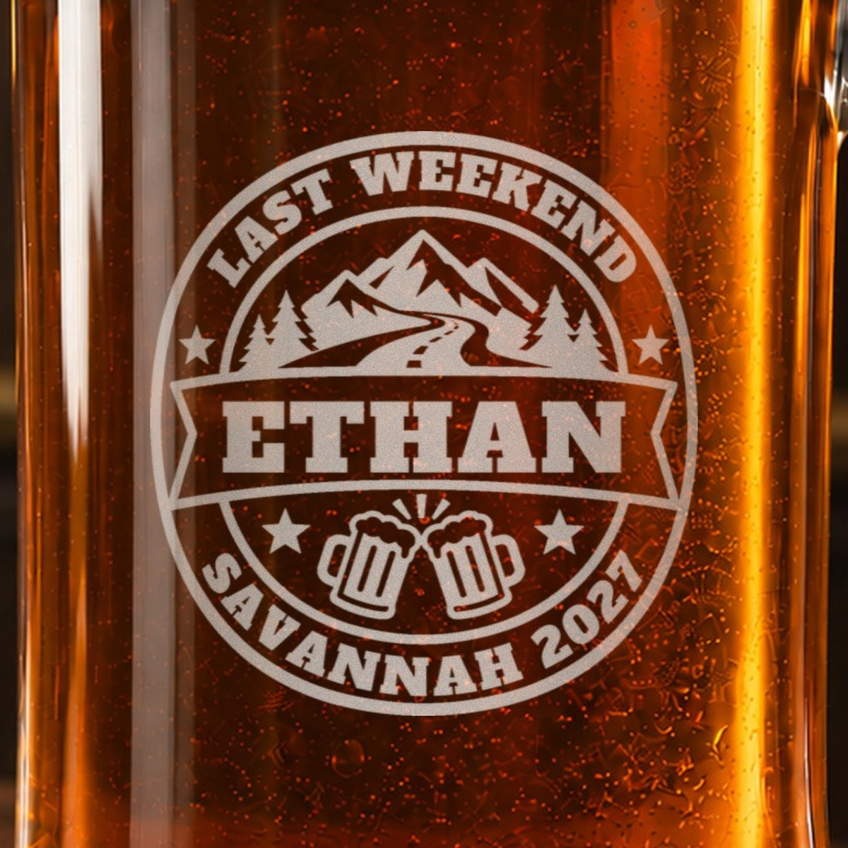 Close-up of the frosted bachelor party badge engraving: mountains, a winding road and toasting mugs, Last Weekend, Ethan and Savannah 2027