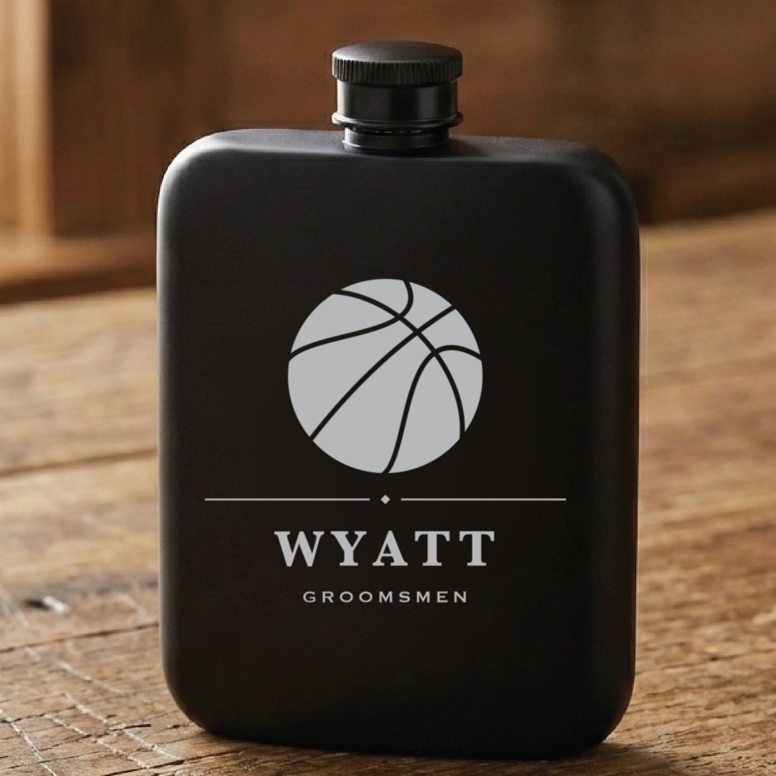 Matte black basketball groomsmen flask laser engraved with a seamed basketball, the name Wyatt and the word Groomsmen beneath it.