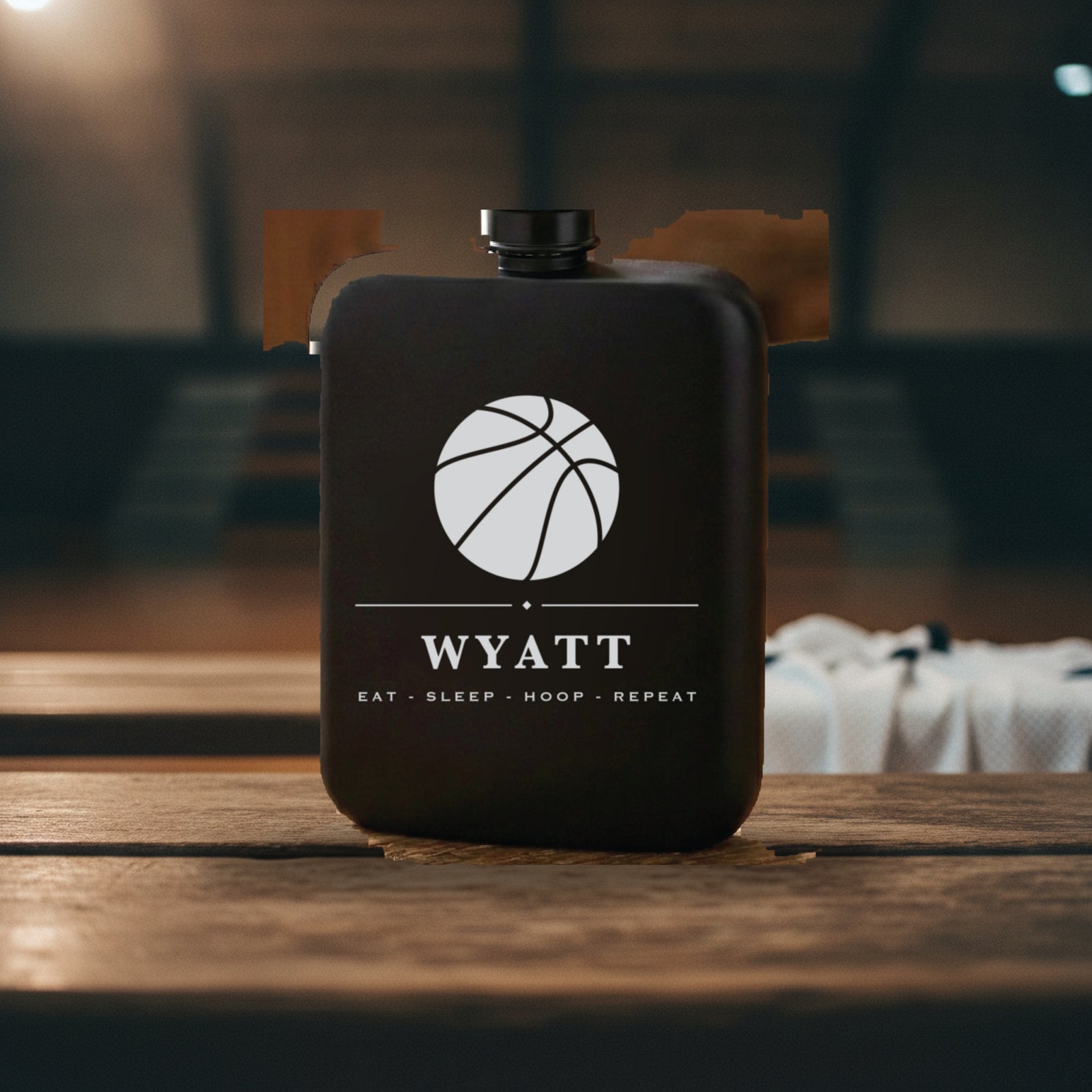Engraved basketball groomsmen flask reading Eat Sleep Hoop Repeat standing on a worn wooden gym bench against a cinder block wall.
