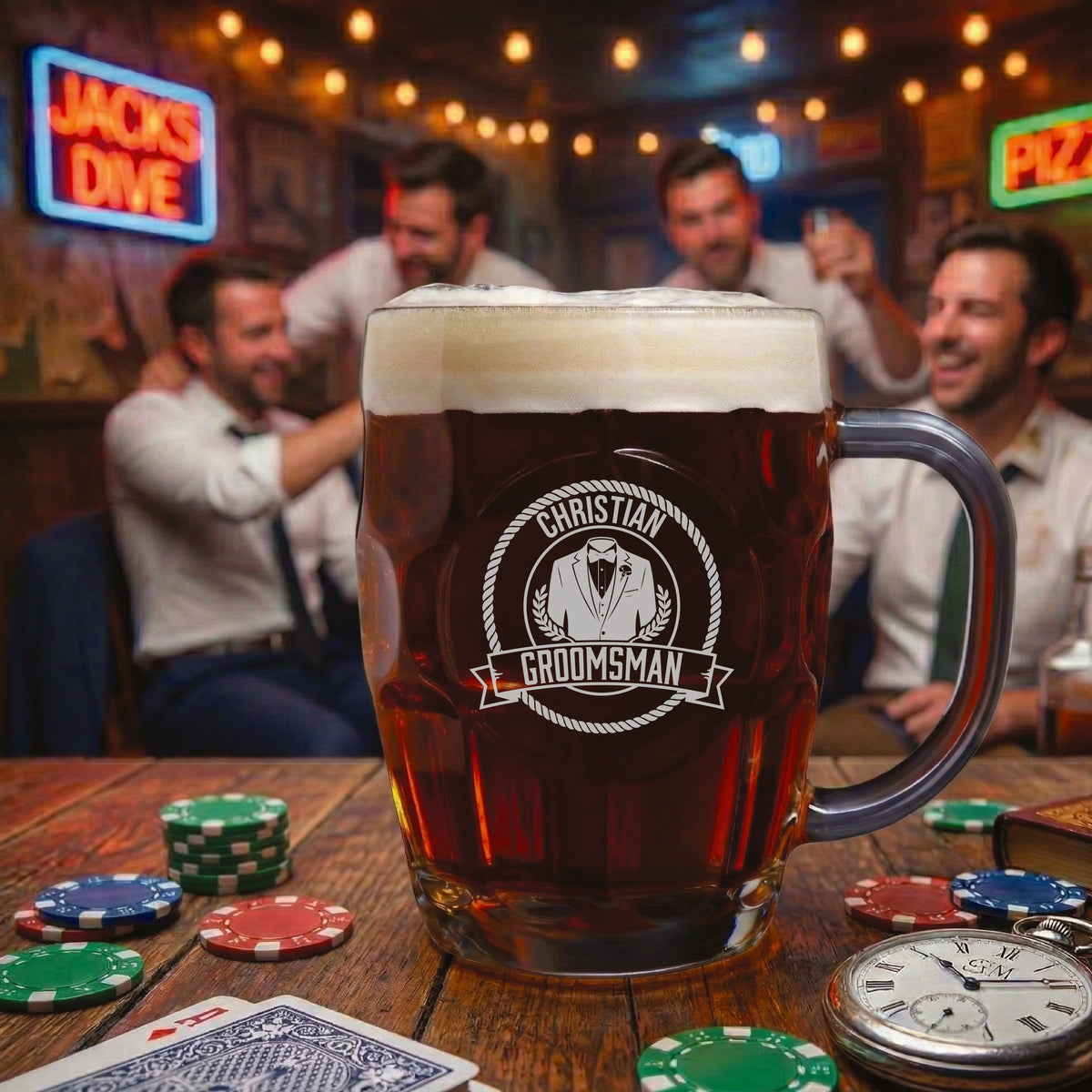 Beer mug filled with dark beer and cream foam head, engraved with sample "Groomsman" design featuring tuxedo and banner motif, displayed on bar table with poker chips and pocket watch.