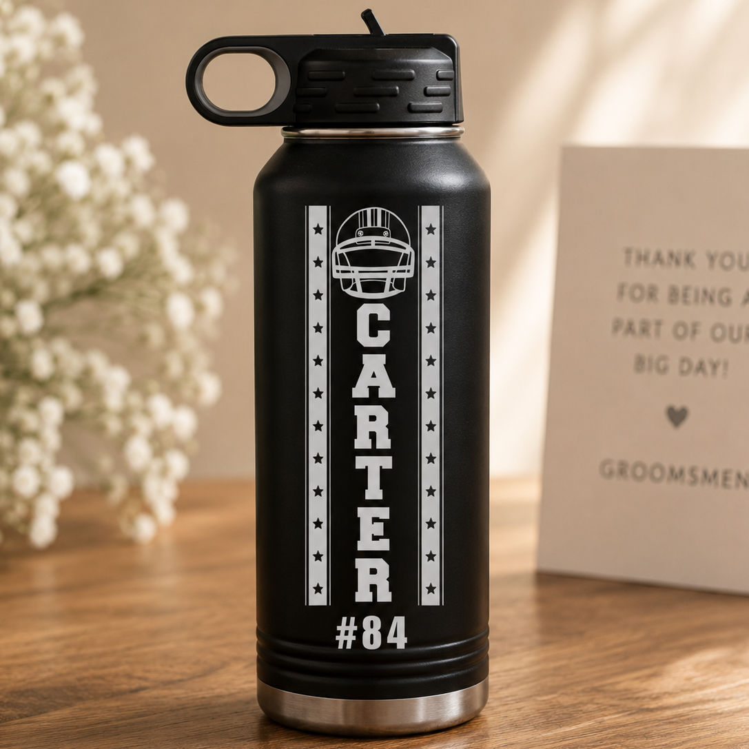 Black insulated water bottle engraved with sample football helmet design, "CARTER" text, number #84, and decorative stars, displayed with wedding stationery and white flowers.