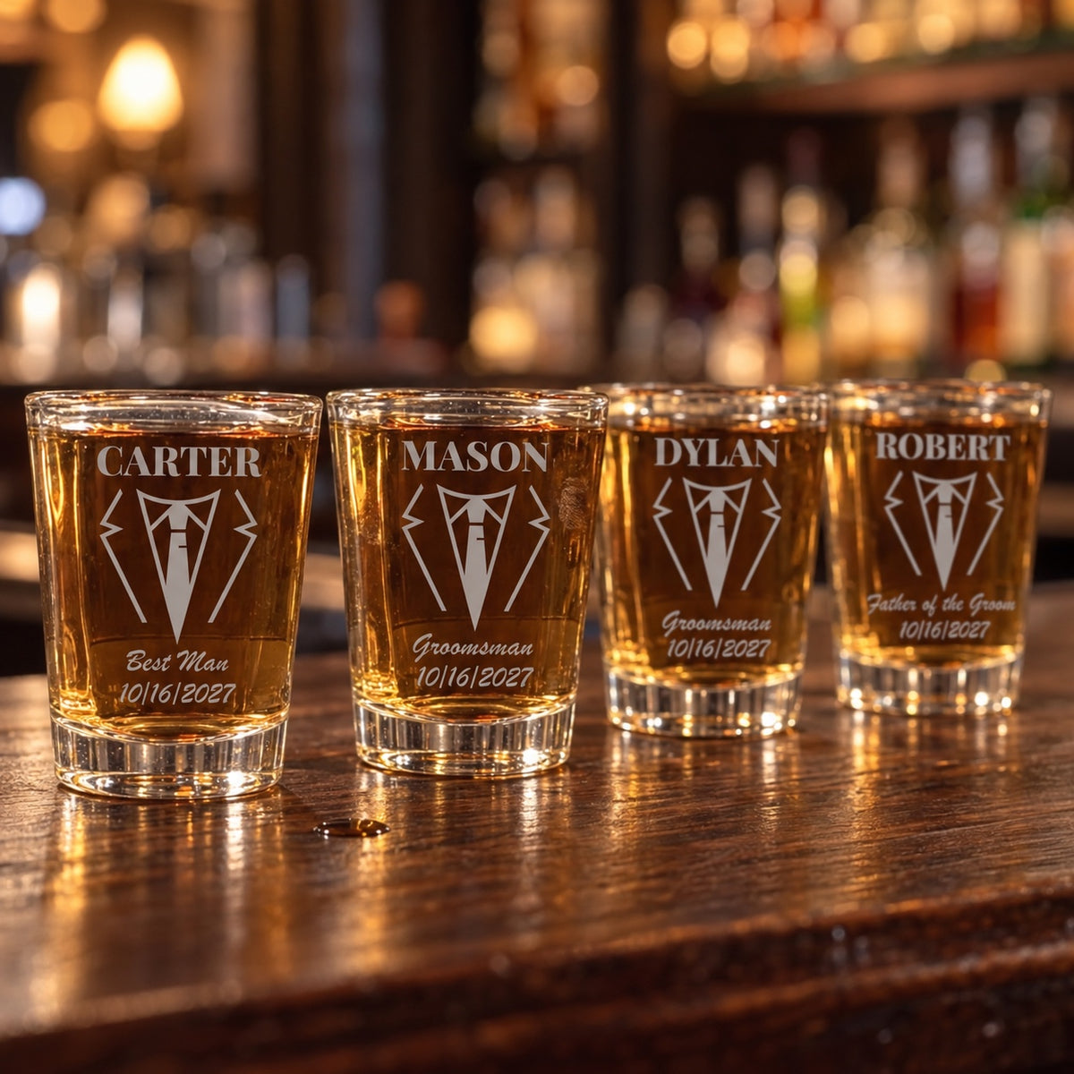 Four groomsmen shot glasses on a bar, each engraved with a name above a tuxedo and tie, a role in script and the date 10/16/2027, for Carter, Mason, Dylan and Robert