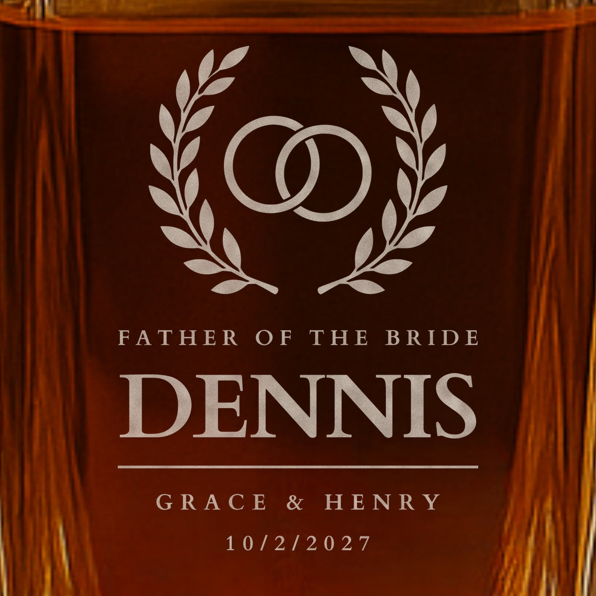 Close-up of frosted engraving on a father of the bride whiskey decanter: rings in a laurel wreath, the name Dennis, Grace and Henry and the date 10/2/2027