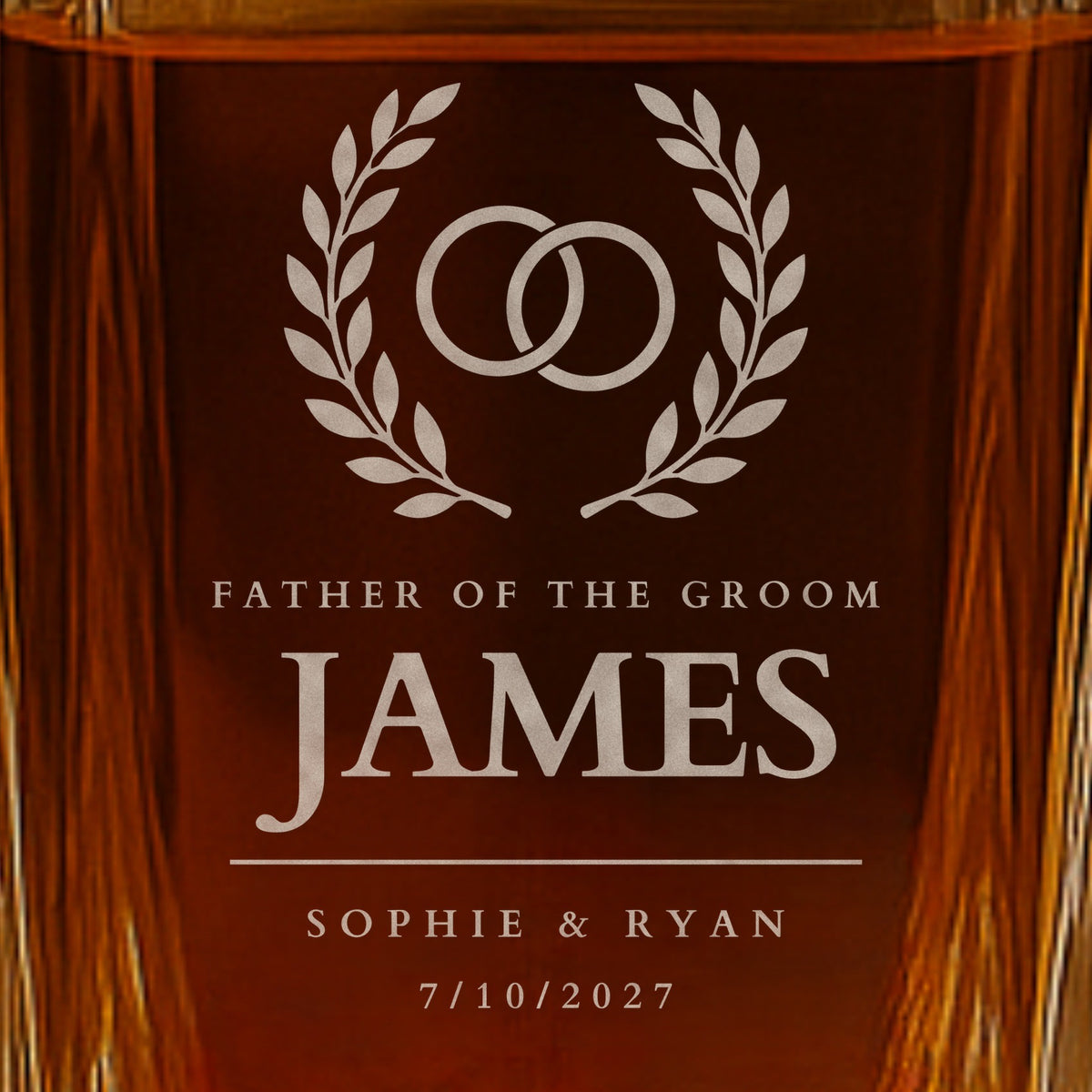 Close-up of frosted engraving on a father of the groom whiskey decanter: rings in a laurel wreath, the name James, Sophie and Ryan and the date 7/10/2027