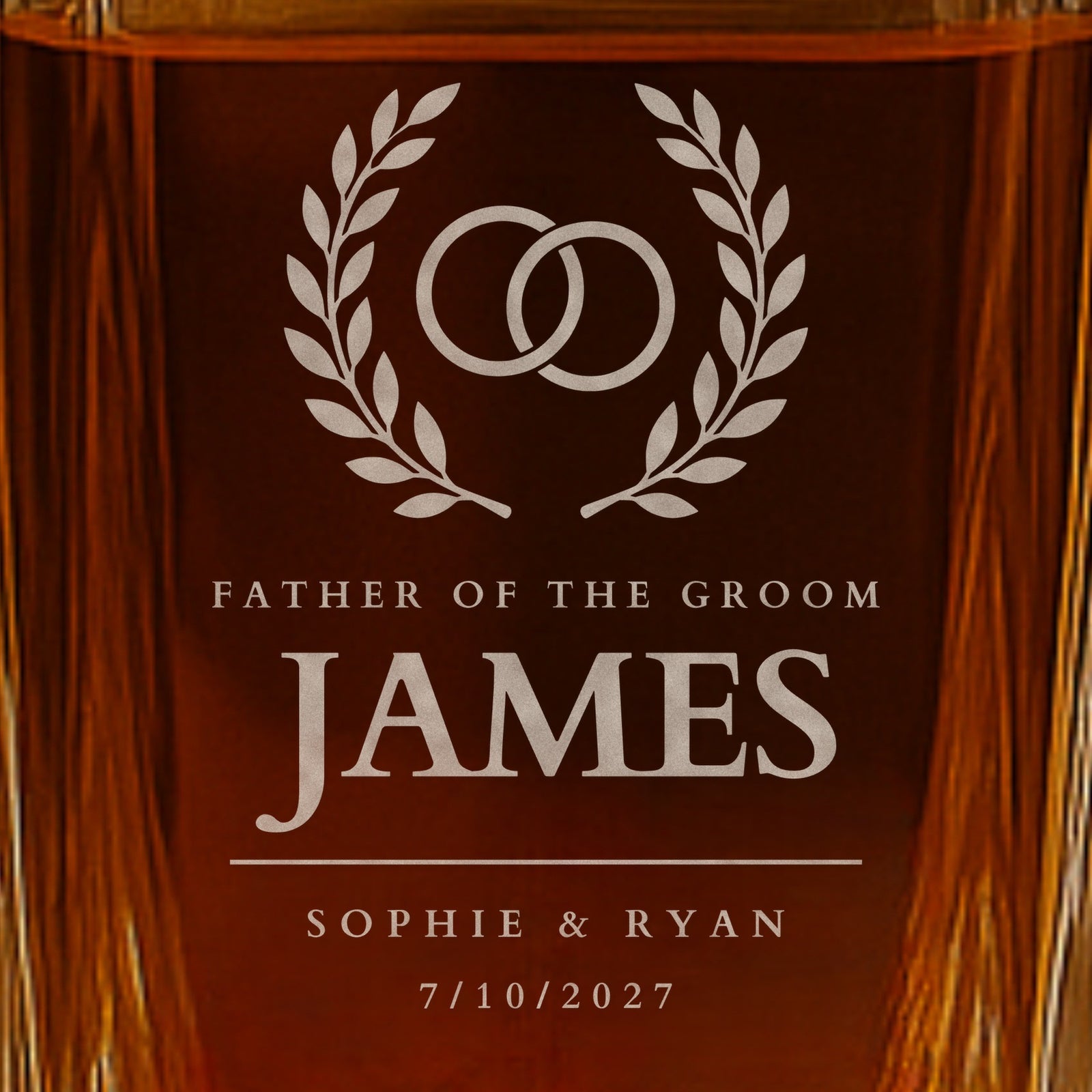 Close-up of frosted engraving on a father of the groom whiskey decanter: rings in a laurel wreath, the name James, Sophie and Ryan and the date 7/10/2027