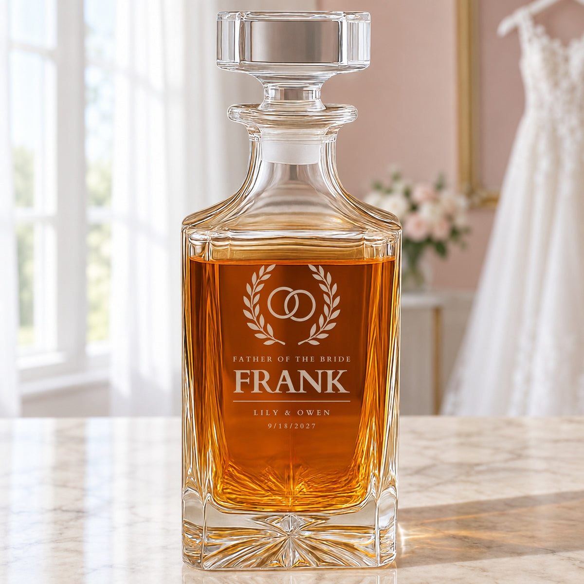 Front of a personalized father of the bride whiskey decanter in a bridal suite: rings in a laurel wreath, the name Frank, Lily and Owen and the date 9/18/2027