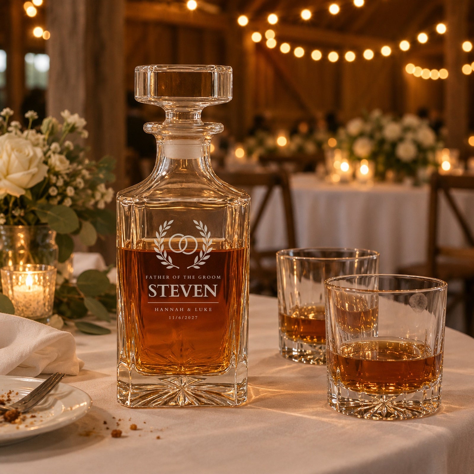 Father of the groom whiskey decanter on a reception table during the toasts, engraved Steven with Hannah and Luke and 11/6/2027, beside two rocks glasses