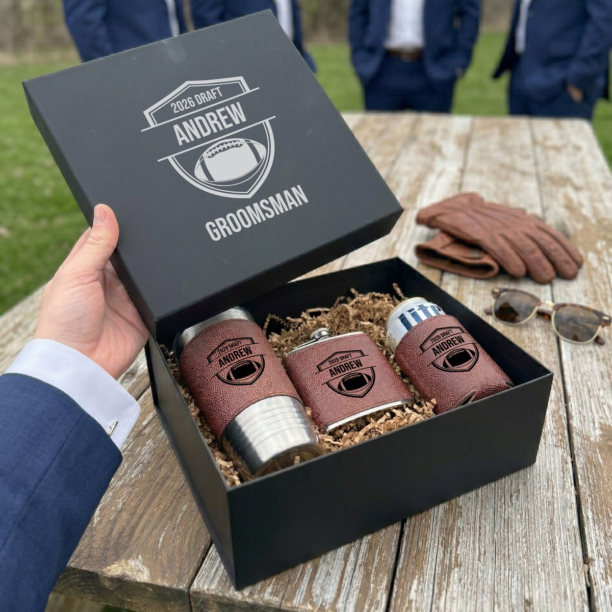 Charcoal gift box open to reveal brown leather flask, two matching koozies, and straw, all engraved with sample name "Andrew" and football motif design