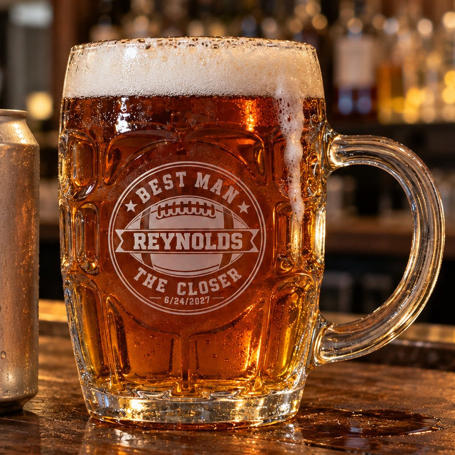 Personalized football groomsmen beer stein filled with ale beside a 12 oz can on a bar top, showing the 20 oz size and the engraved football crest