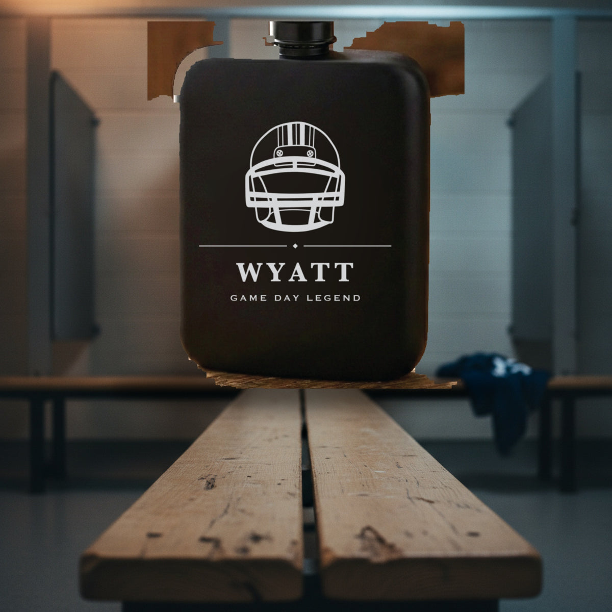 Engraved football groomsmen flask reading Game Day Legend standing on a worn wooden locker room bench with stall dividers behind.