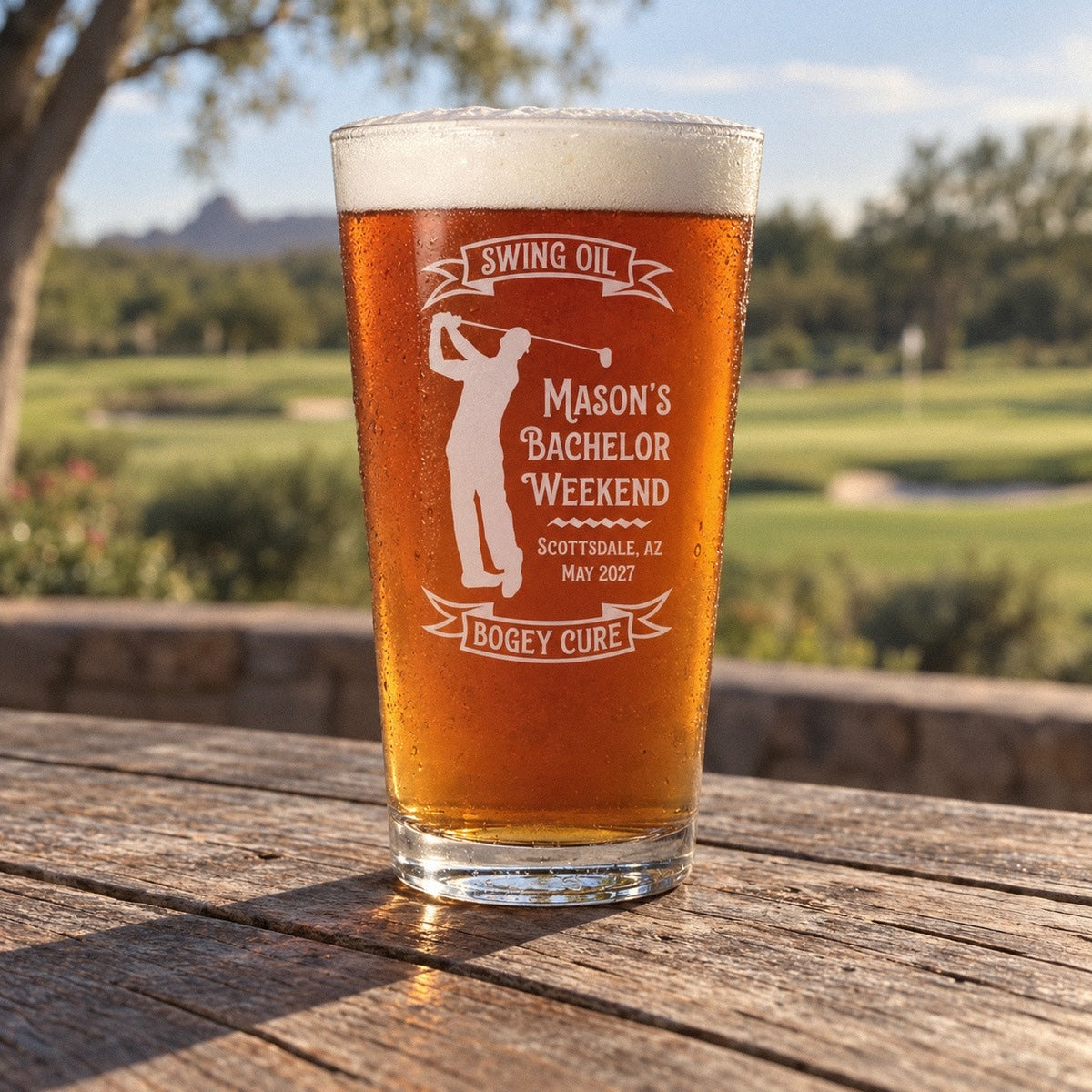 Golf bachelor party pint glass with a Swing Oil banner, a golfer mid-swing and MASON'S BACHELOR WEEKEND, SCOTTSDALE, AZ, MAY 2027 on a clubhouse terrace
