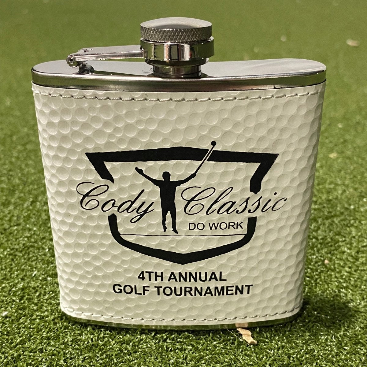Real photo of the golf ball flask engraved with a customer logo, the Cody Classic 4th Annual Golf Tournament, showing the upload-your-logo option.