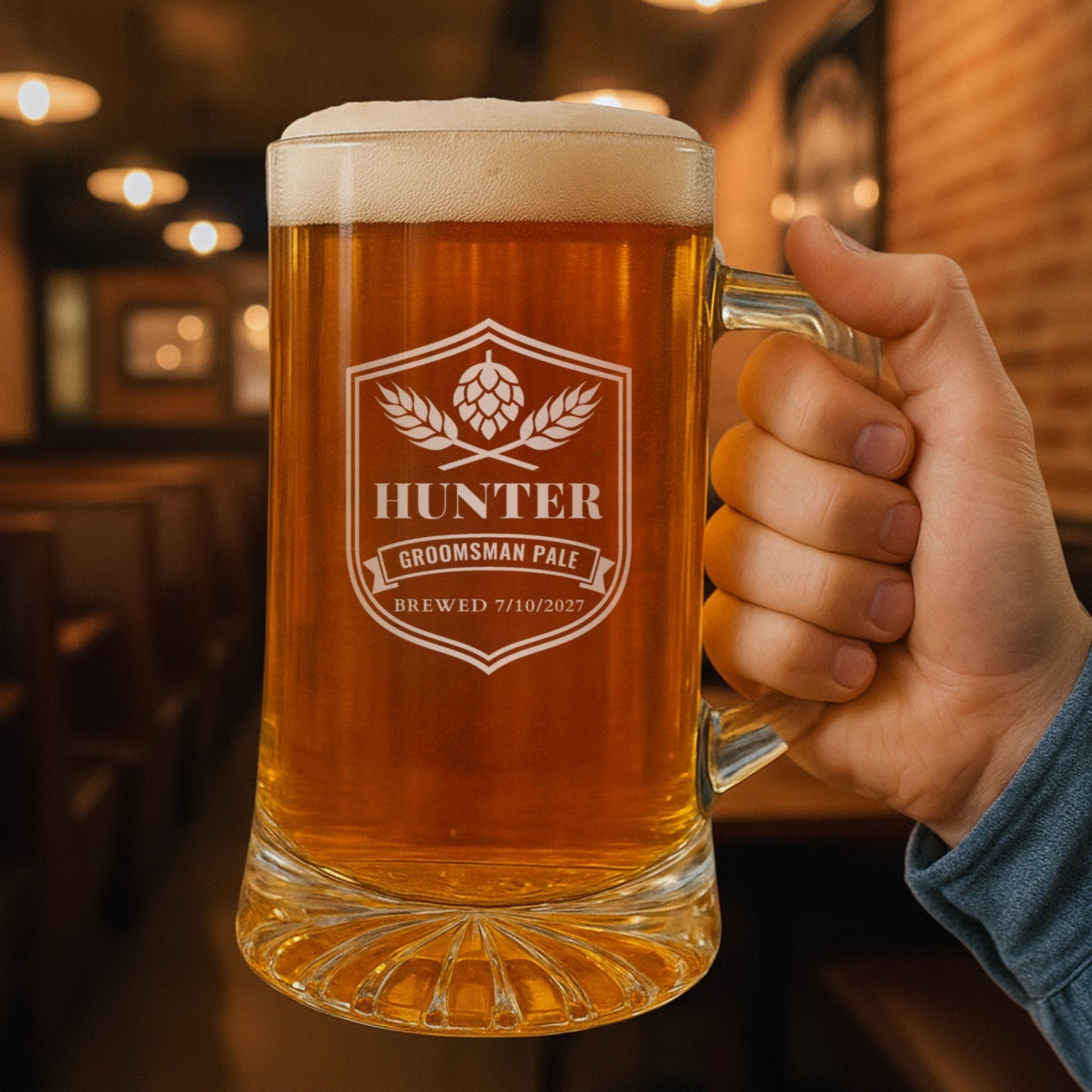 Hand holding a 25 oz personalized groomsmen beer stein in a pub, engraved like a craft beer label with Hunter, Groomsman Pale and Brewed 7/10/2027