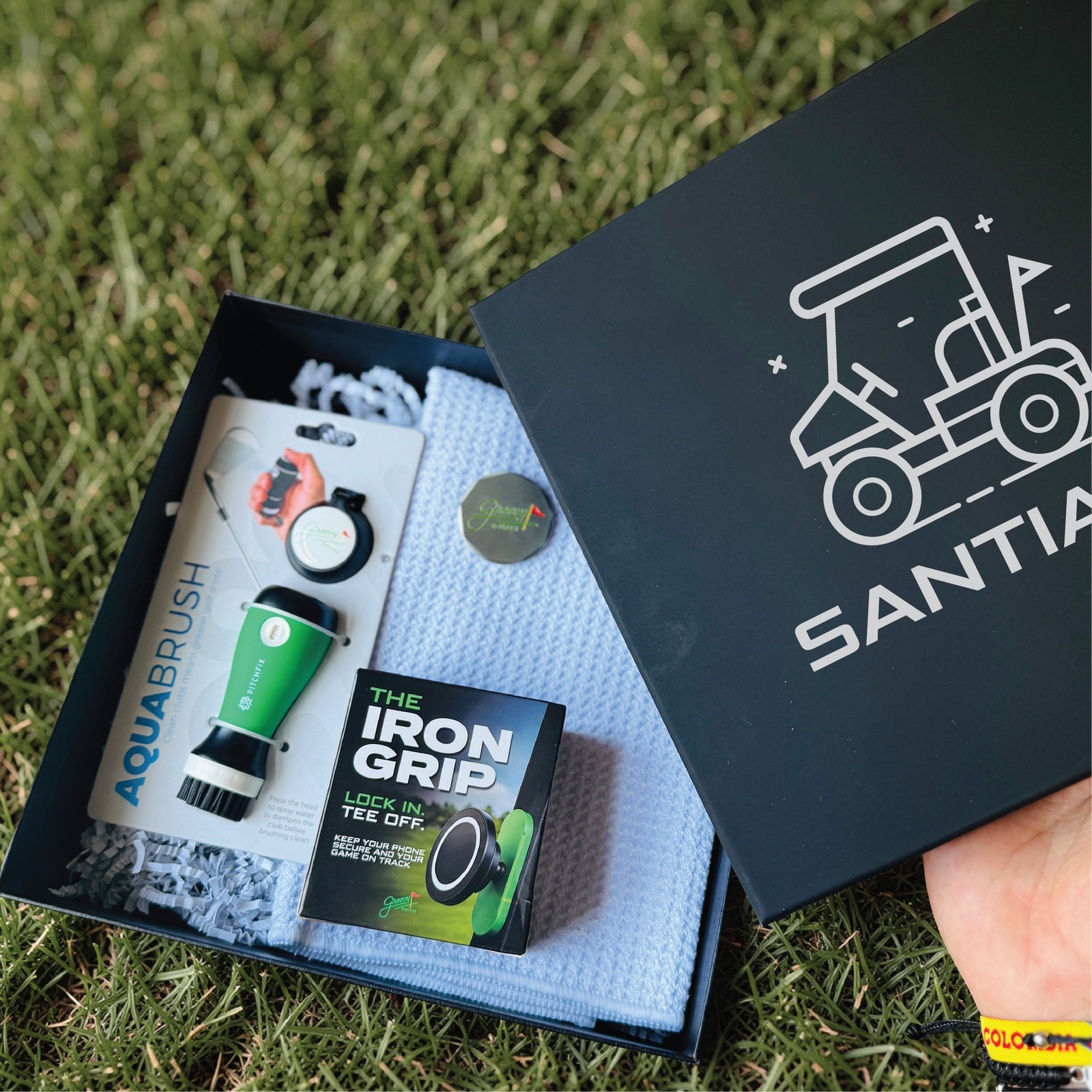 Personalized groomsman golf gift box with a name-engraved navy lid, open to show the club cleaner, waffle towel, ball marker and magnetic phone mount.