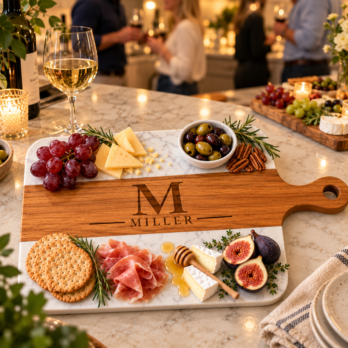 Engraved monogram charcuterie board with M and MILLER on a marble kitchen island at an evening party with wine, a wedding gift for the bride and groom to host with