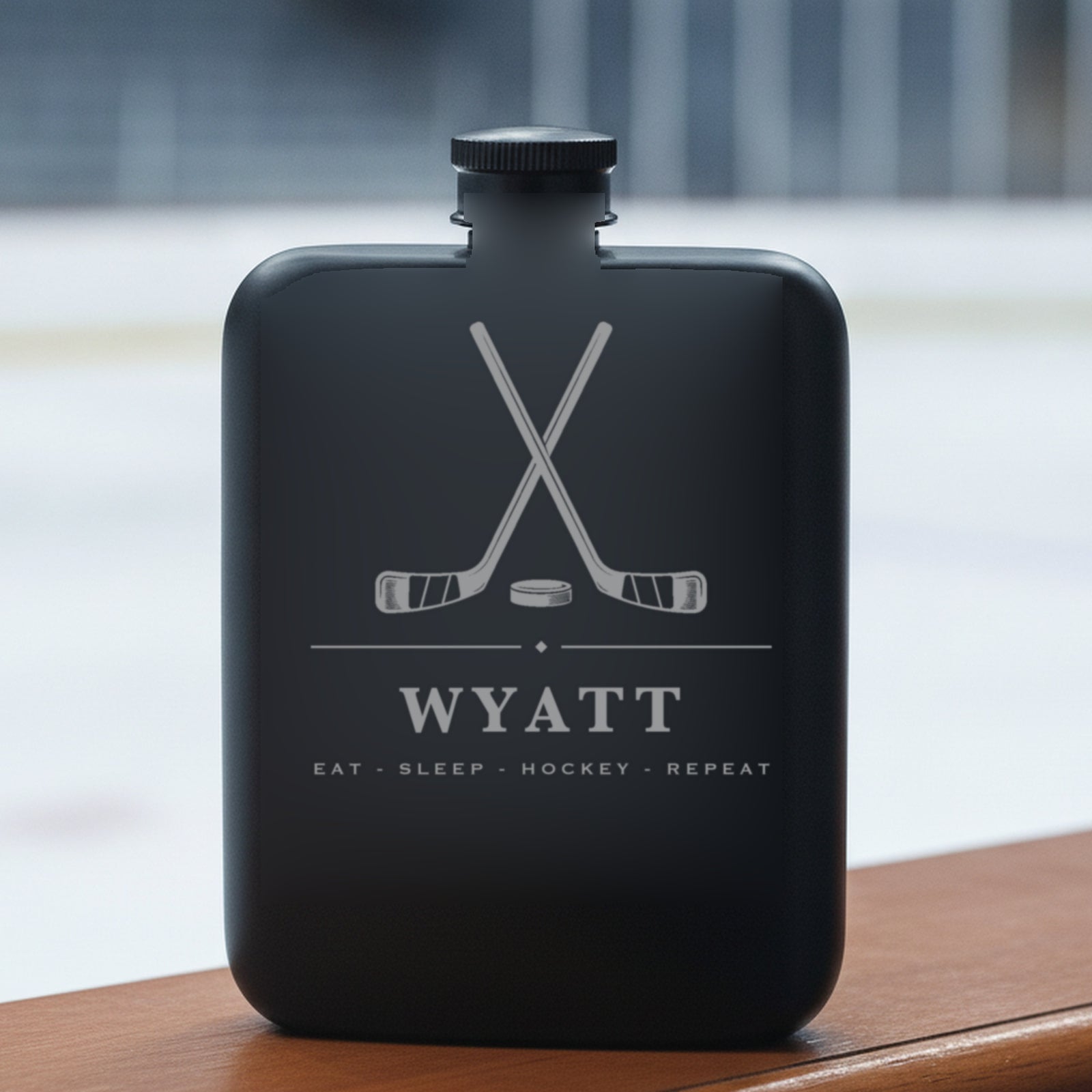 Personalized hockey groomsmen flask reading Eat - Sleep - Hockey - Repeat resting on a dasher board with the ice surface behind it.