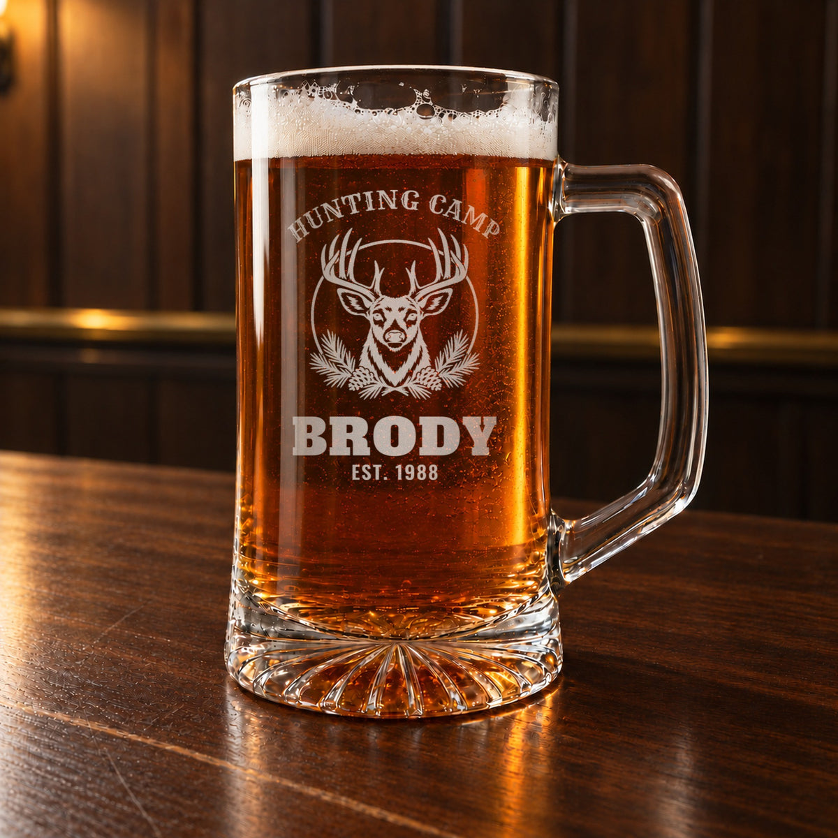 Personalized hunting camp beer stein on a walnut bar, engraved with a whitetail buck and pine boughs: Hunting Camp, Brody, Est. 1988