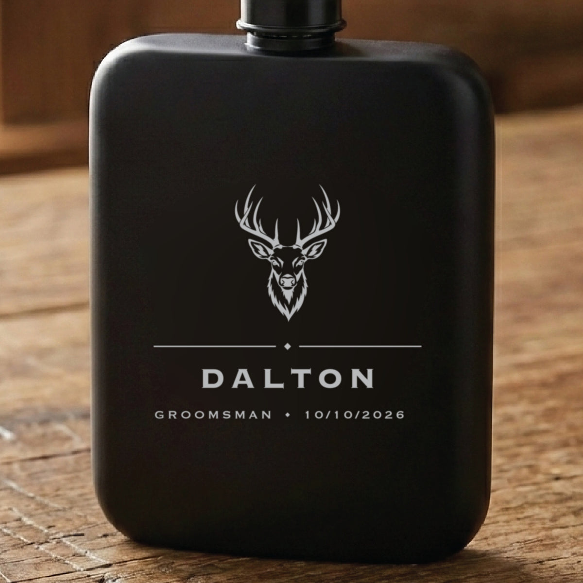 Matte black hunting groomsmen flask laser engraved with a whitetail buck above the name Dalton, his role and the wedding date.