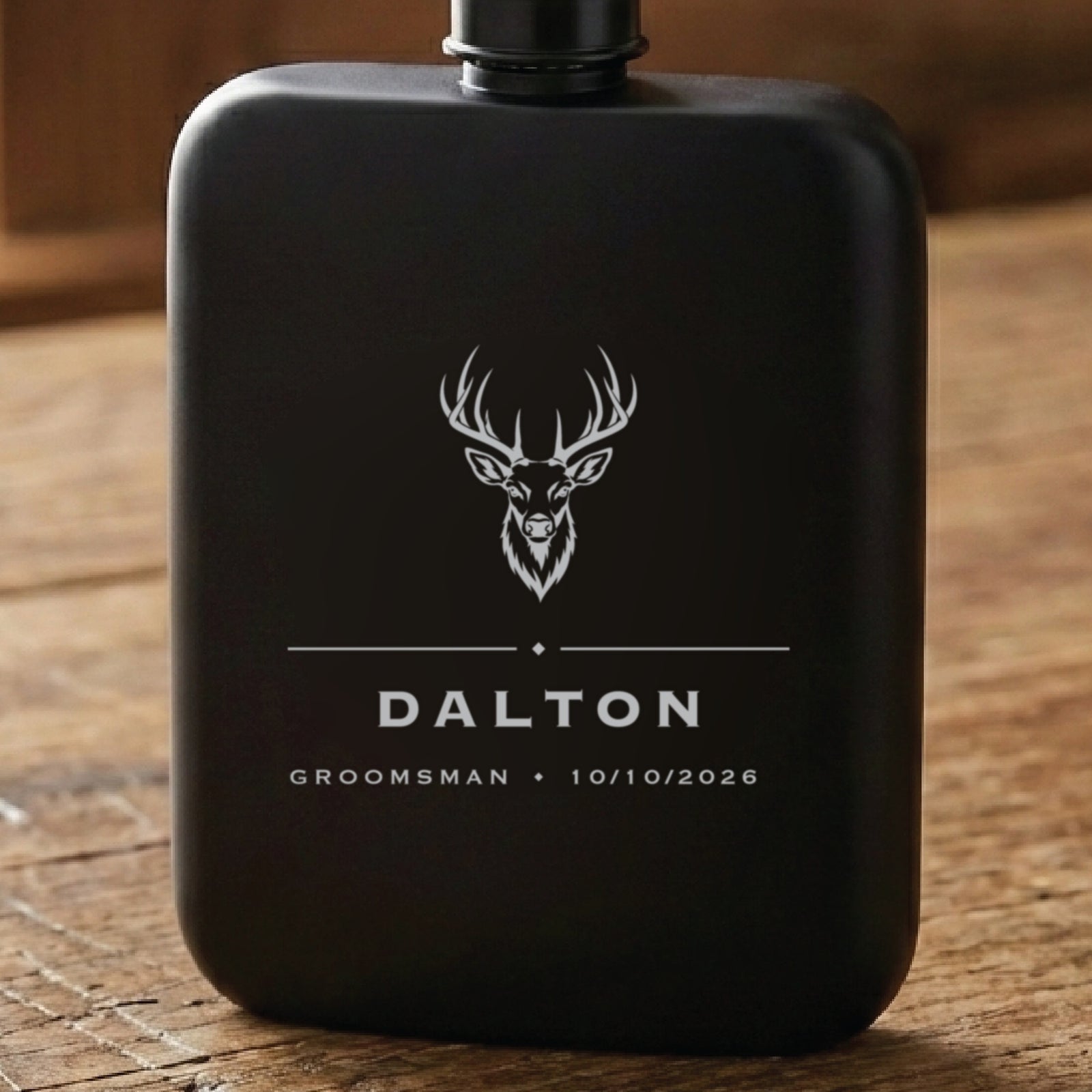 Matte black hunting groomsmen flask laser engraved with a whitetail buck above the name Dalton, his role and the wedding date.