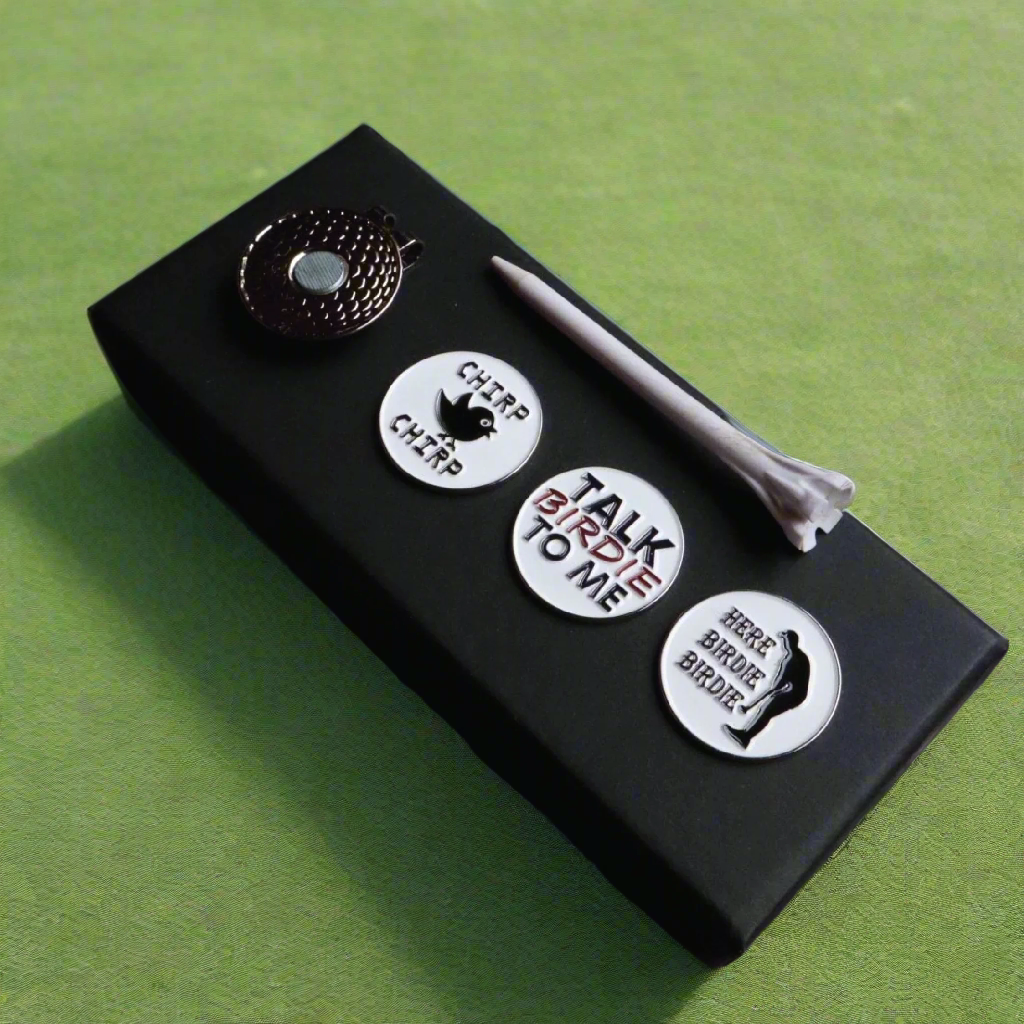 Black cigar accessory set displayed on green surface, featuring metal cutter tool at top and three white circular tool heads with sample engravings reading "CHIP CHIP," "TALK BIRDIE TO ME," and "HERE BIRDIE BIRDIE