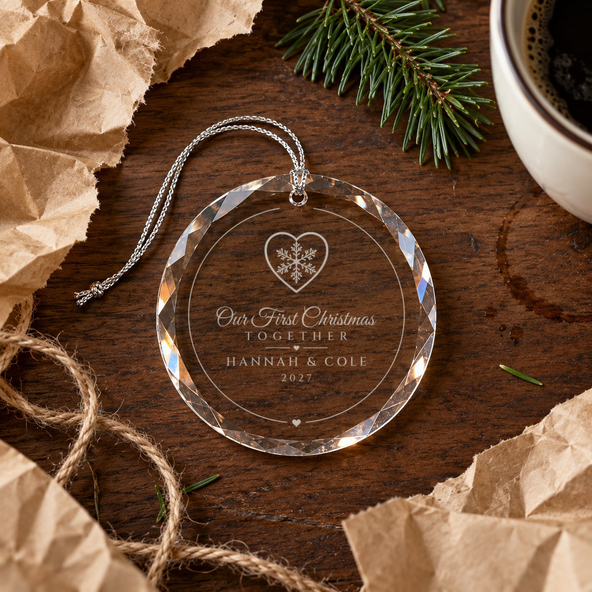 Our First Christmas Together couples ornament just unwrapped from kraft paper on a walnut table, Snowflake Heart design engraved HANNAH &amp; COLE, 2027