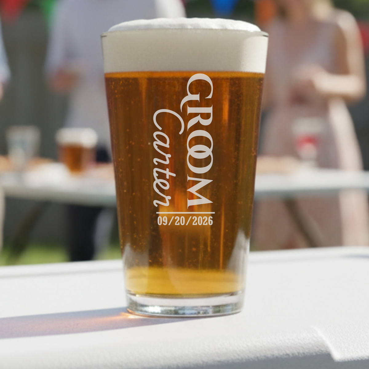 Pint glass filled with amber beer, engraved with sample text "GROOM Grooms Crew" and date "09/20/2026" in white lettering