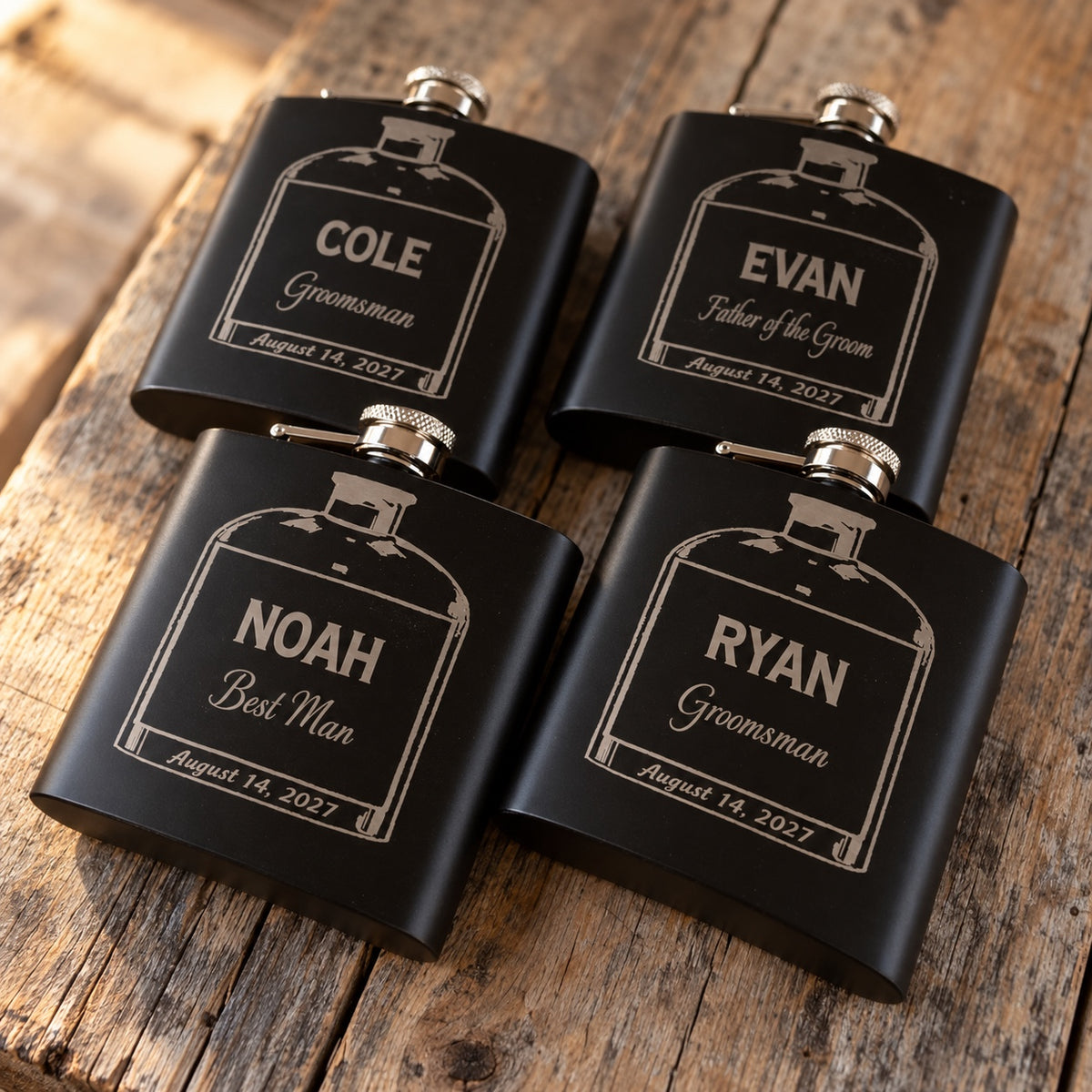 Four personalized groomsmen flasks fanned on a wood table, engraved NOAH Best Man, RYAN and COLE Groomsman and EVAN Father of the Groom.