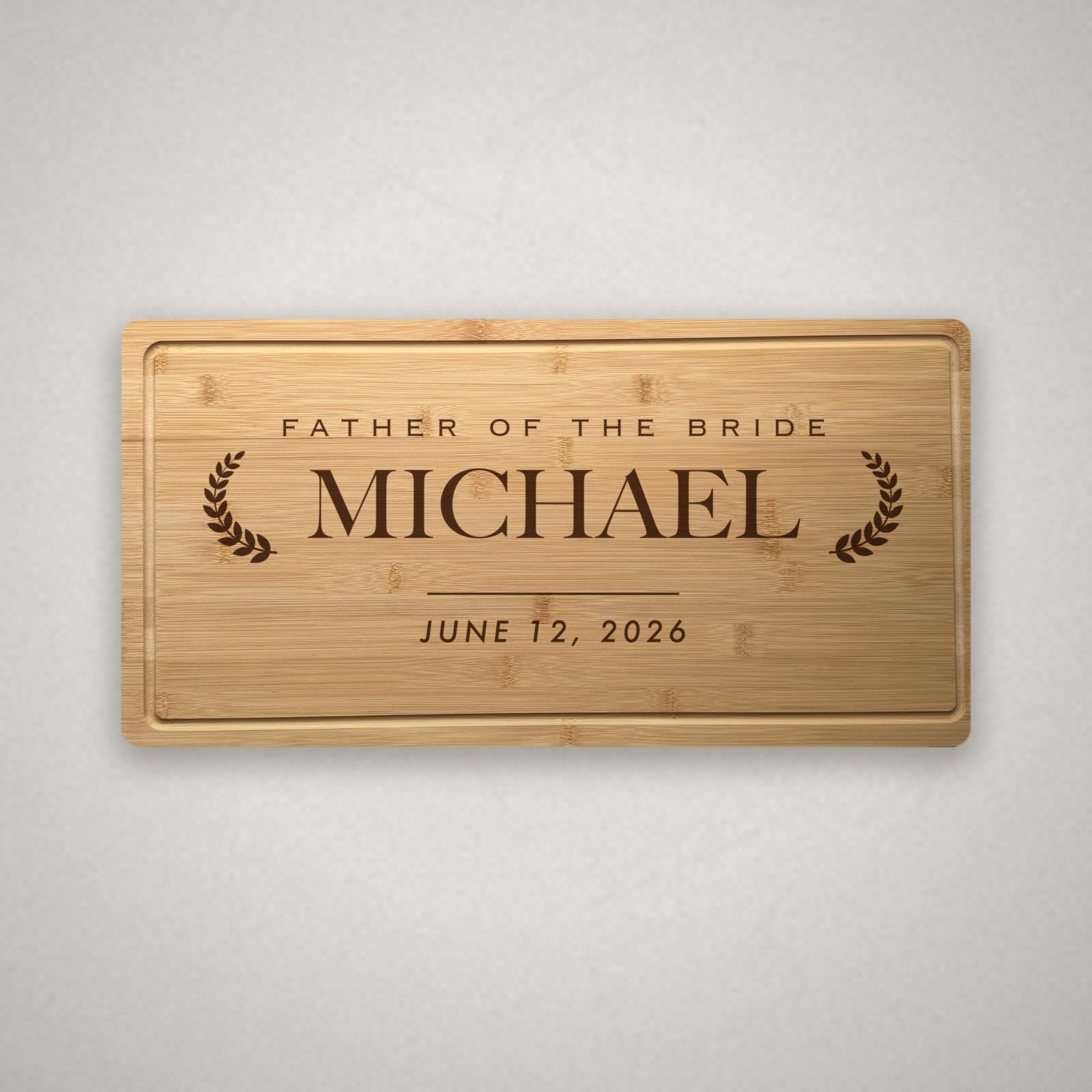 Personalized wedding party cutting board in solid bamboo, engraved Father of the Bride above the name Michael between two laurel branches with the wedding date below.