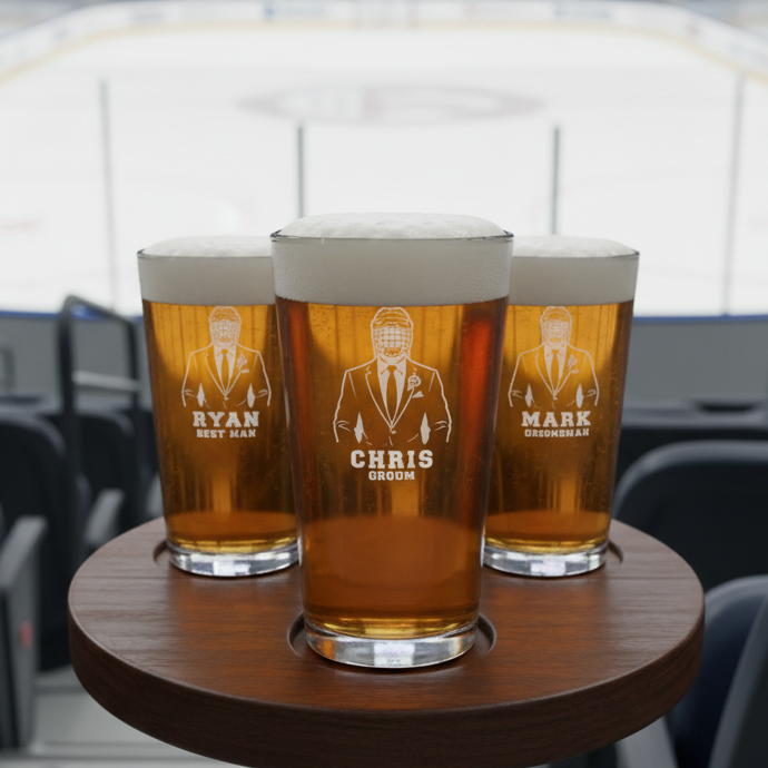Three personalized pint glasses with laser-etched sample names "Ryan Best Man," "Chris Groom," and "Mark Groomsman" filled with beer, displayed on wooden coaster.